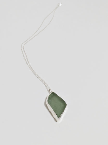 Close up of a big turquoise sea glass pendant with a silver chain on a white background.
