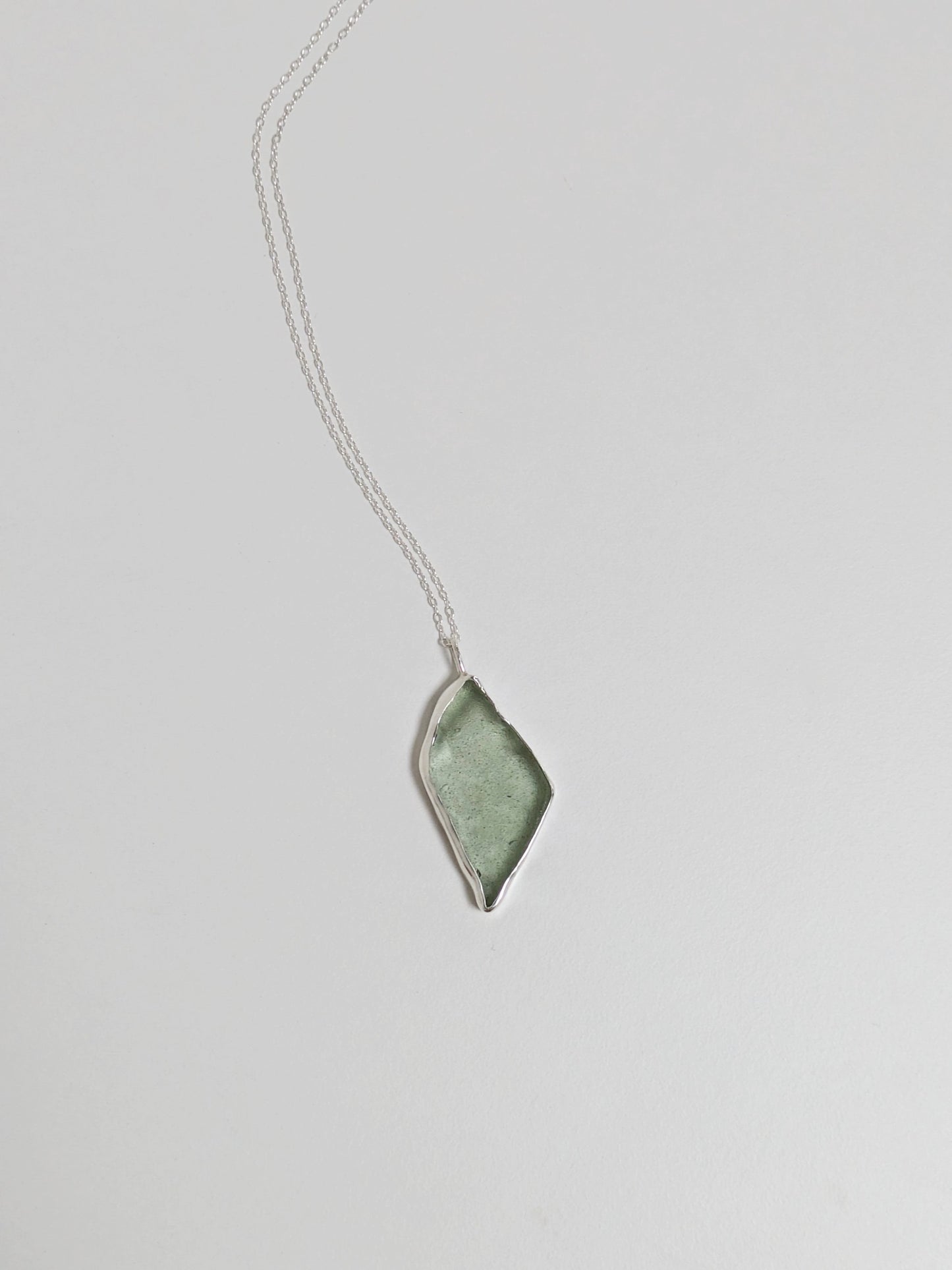 A big turquoise sea glass pendant with a silver chain is central on a white background.