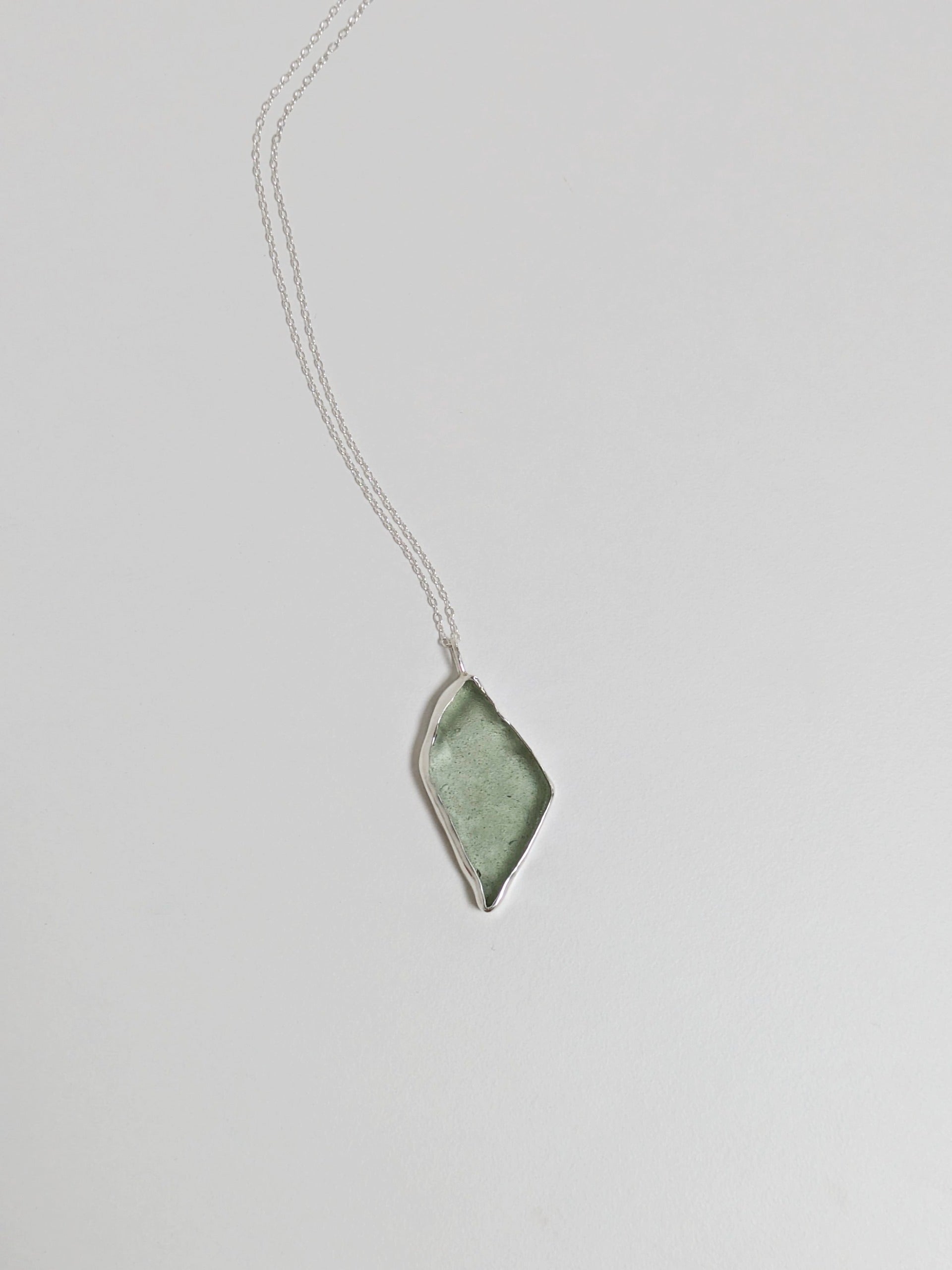 A big turquoise sea glass pendant with a silver chain is central on a white background.
