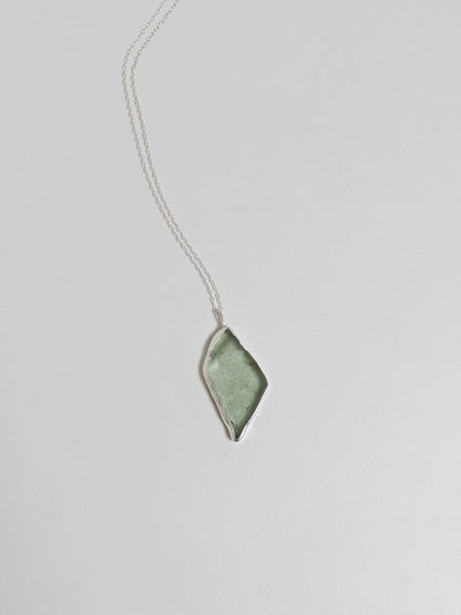 A big turquoise sea glass pendant with a silver chain is central on a white background.