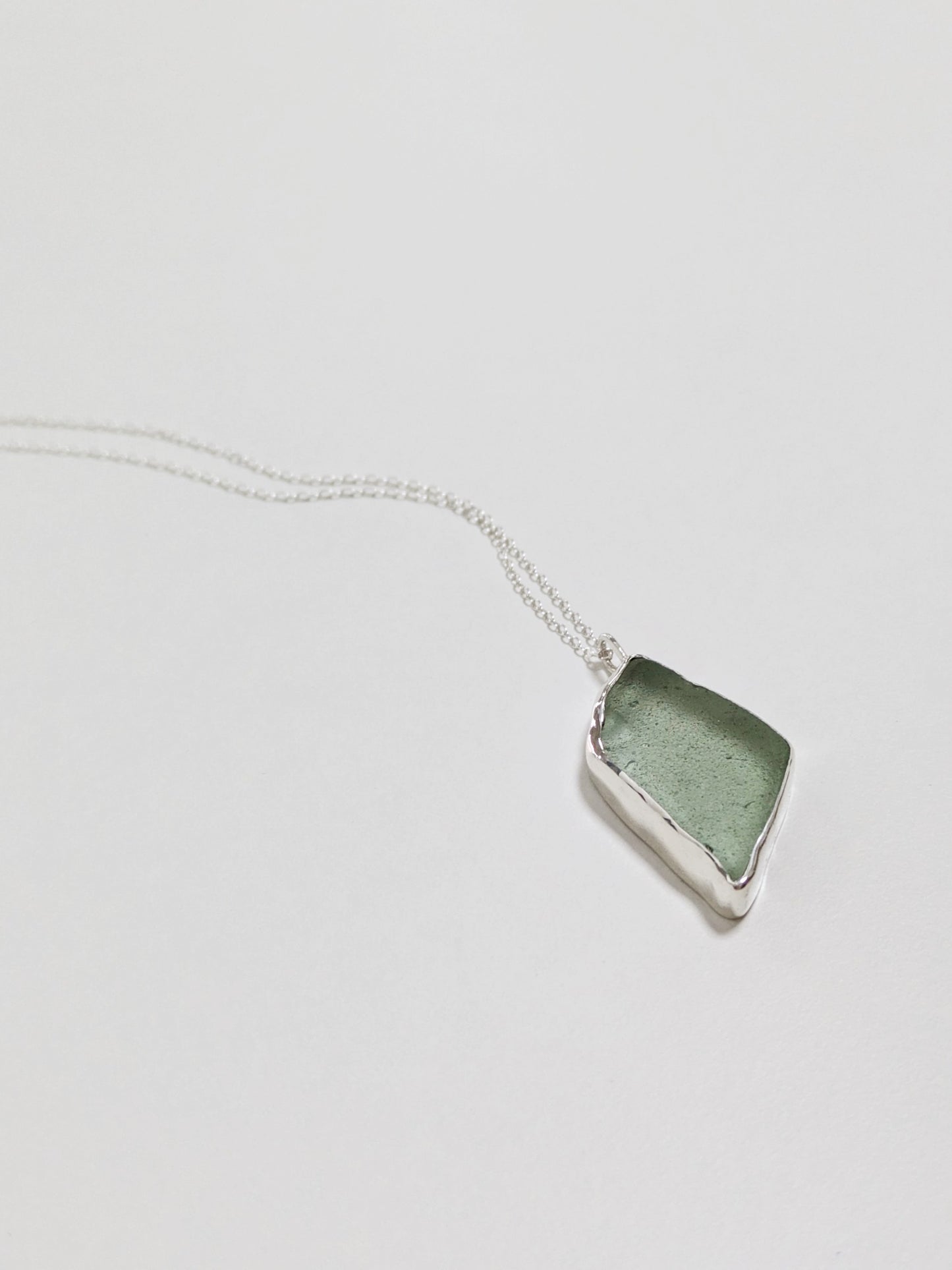 Close up of a big turquoise sea glass pendant with a silver chain on a white background.