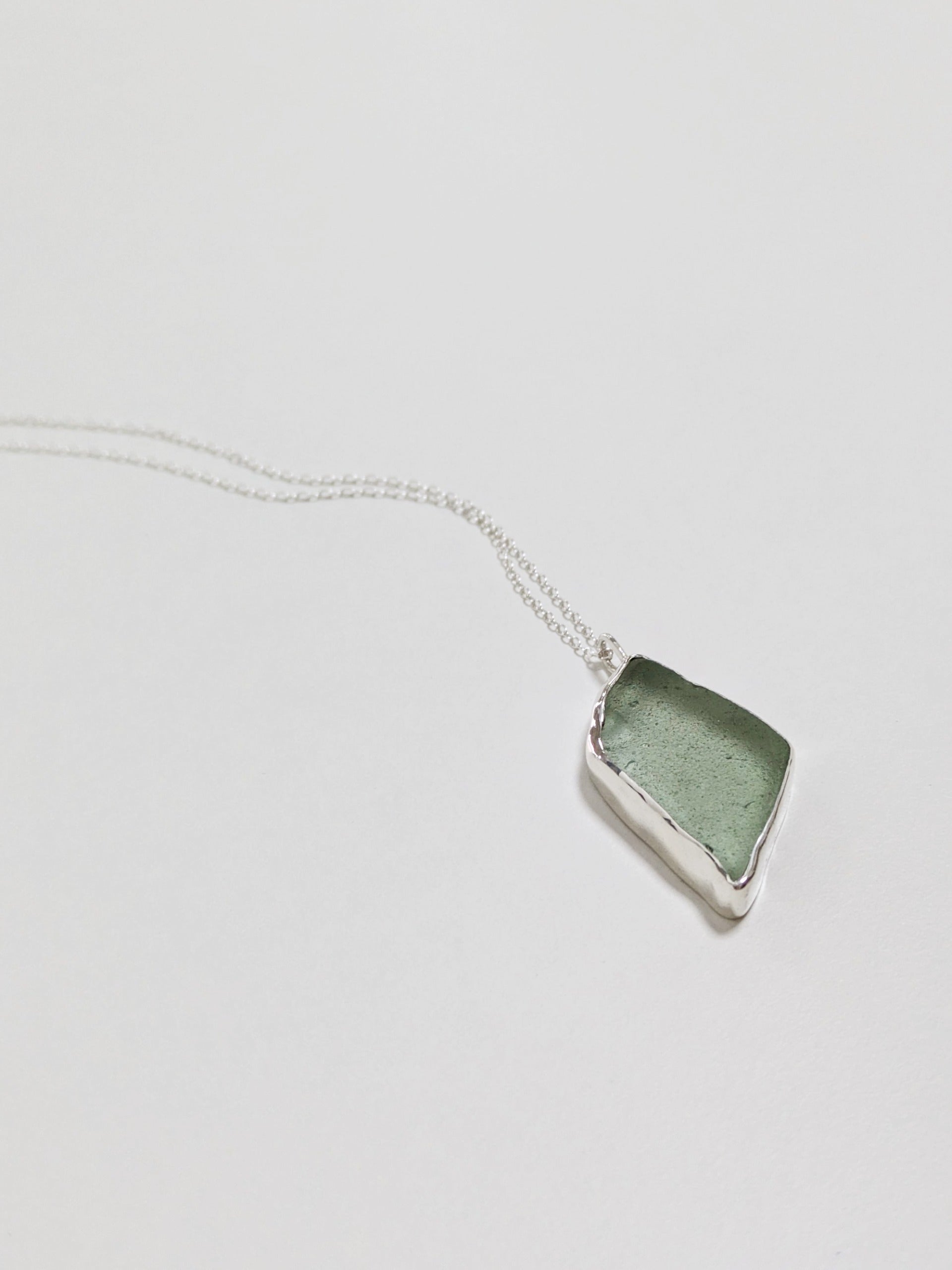 Close up of a big turquoise sea glass pendant with a silver chain on a white background.