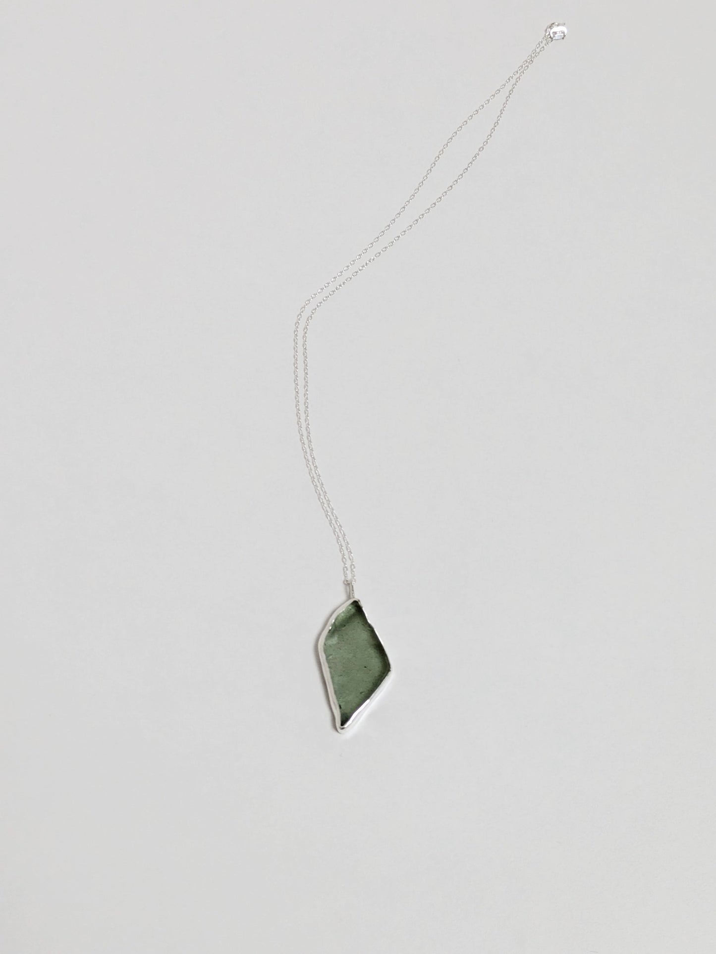 A big turquoise sea glass pendant with a silver chain on a white background.