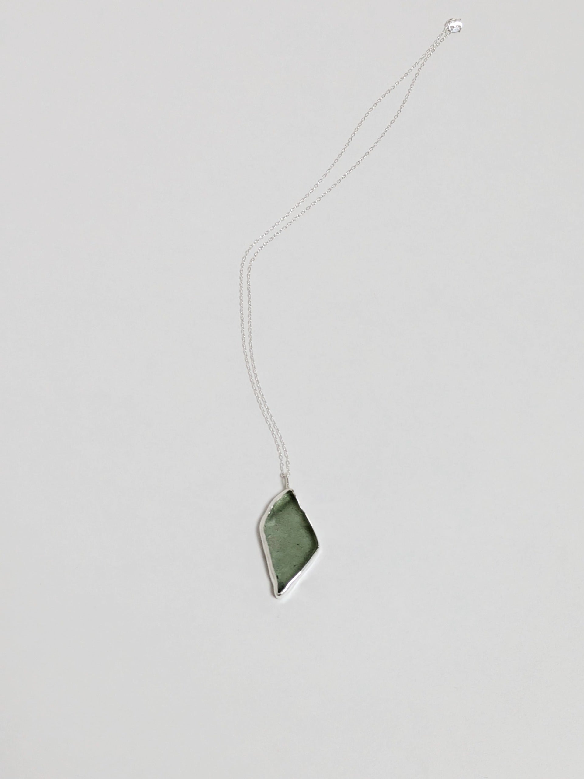 A big turquoise sea glass pendant with a silver chain on a white background.