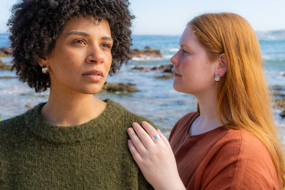 Two women standing close to each other by the ocean wearing hammered hoops