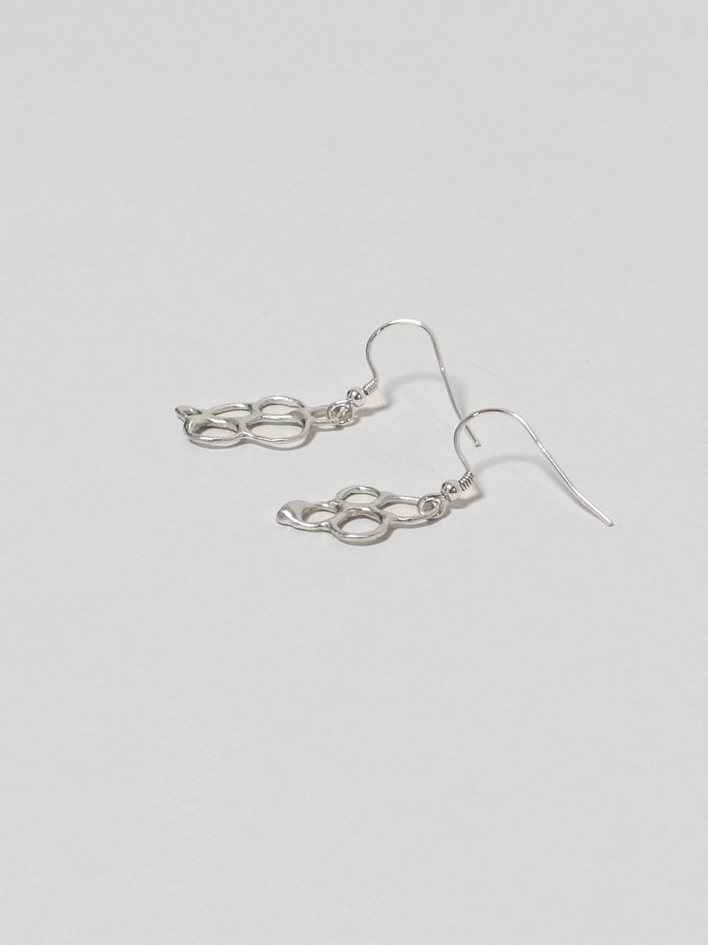 Side view of organic shaped silver drop earrings on white background
