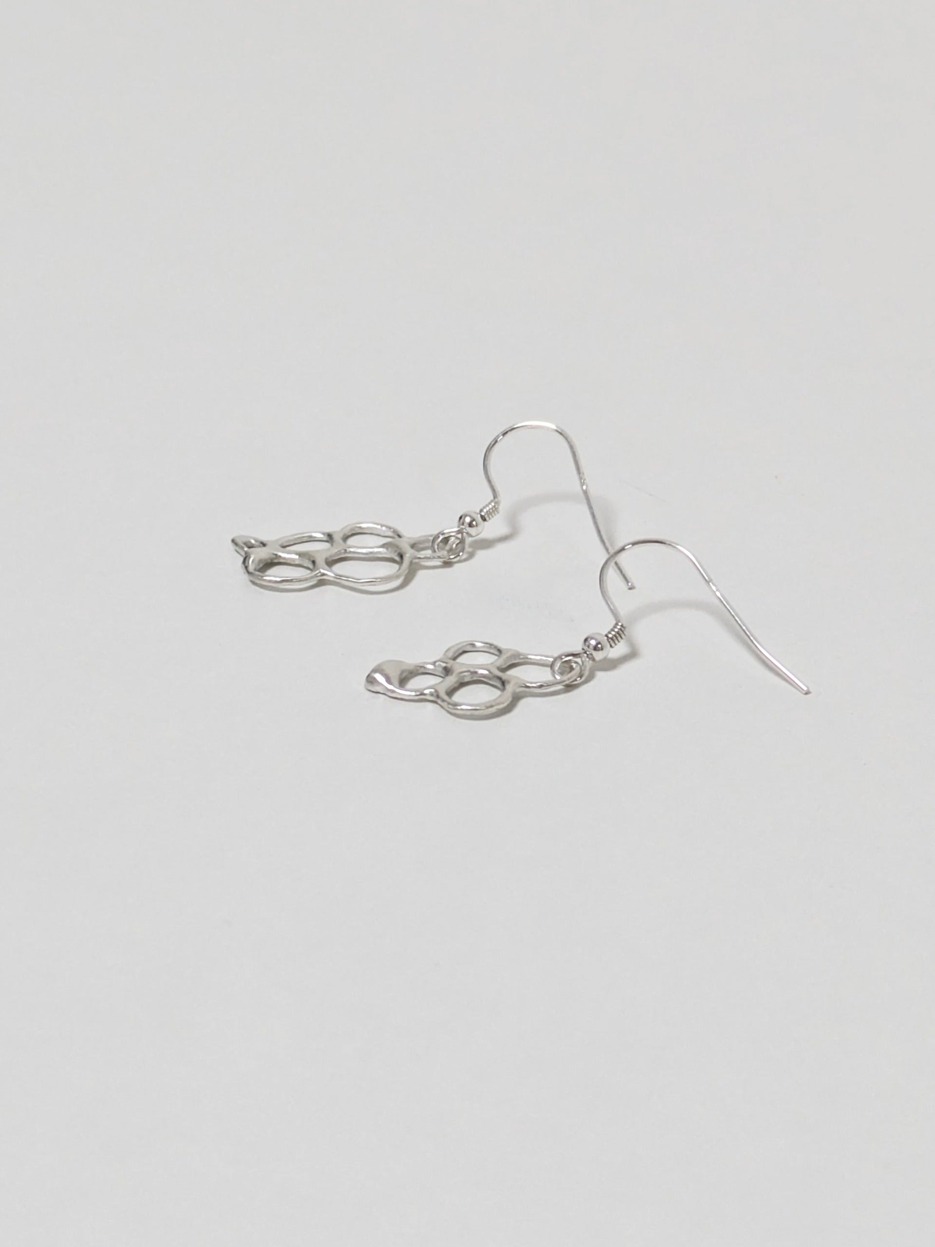 Side view of organic shaped silver drop earrings on white background
