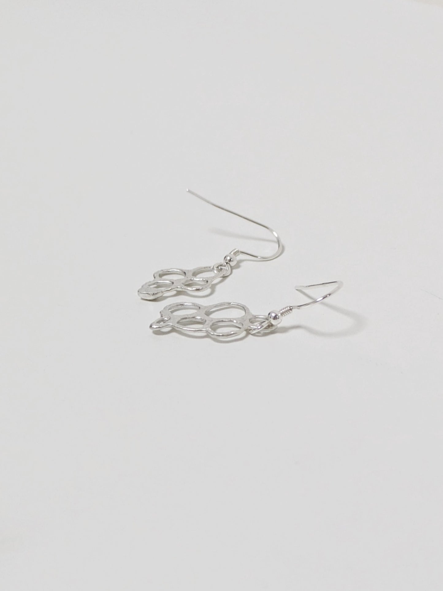 Side view of organic shaped silver drop earrings on white background