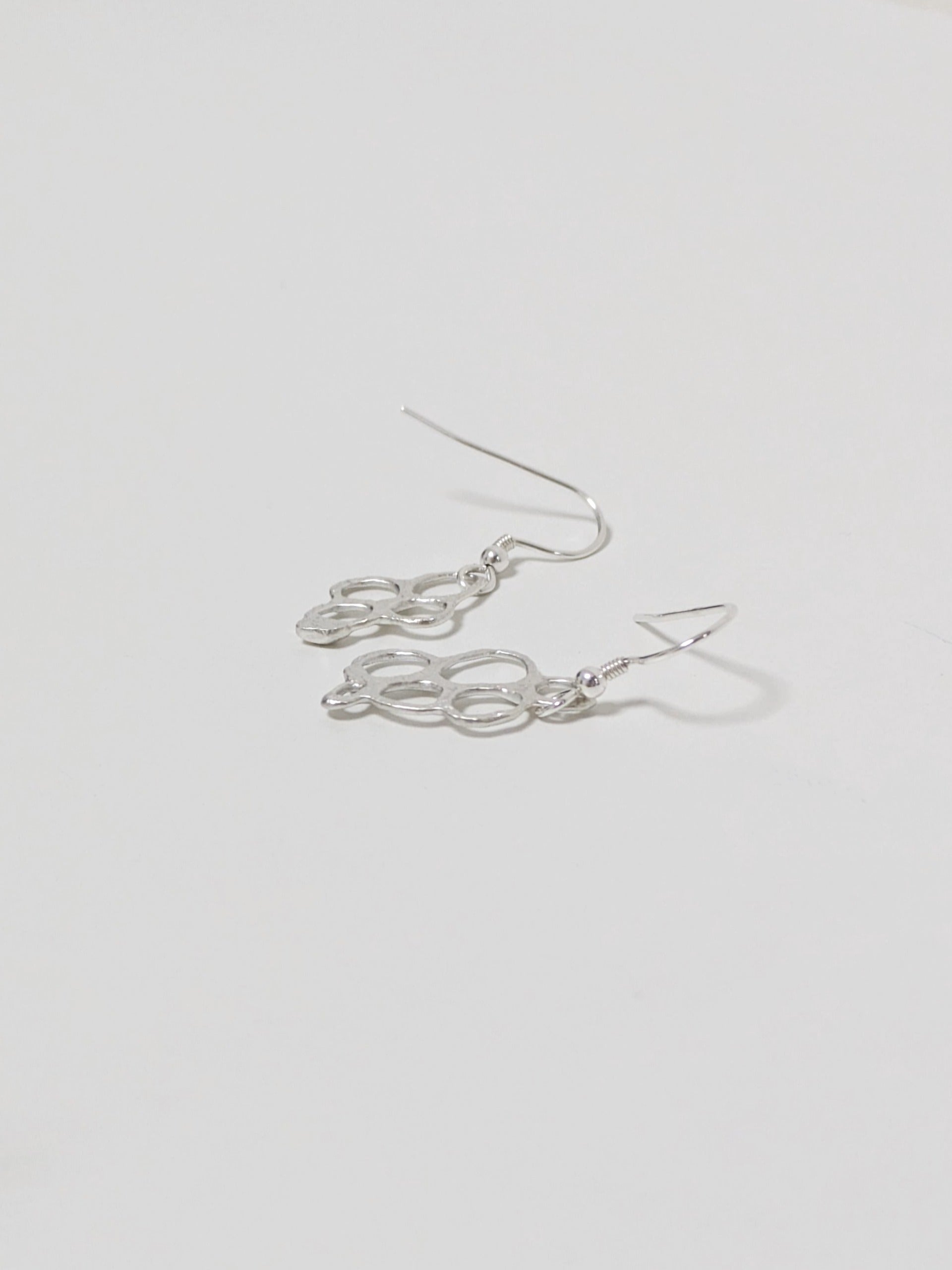 Side view of organic shaped silver drop earrings on white background