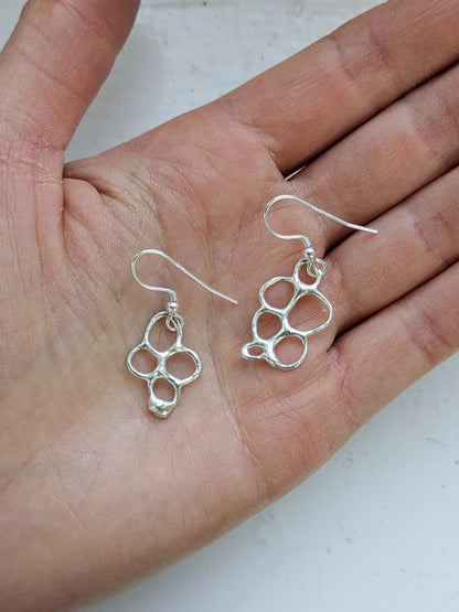 Organic shaped silver drop earrings in palm of a hand