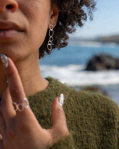 Close up of woman wearing chunky pebble stack earrings with blurred sea in the background