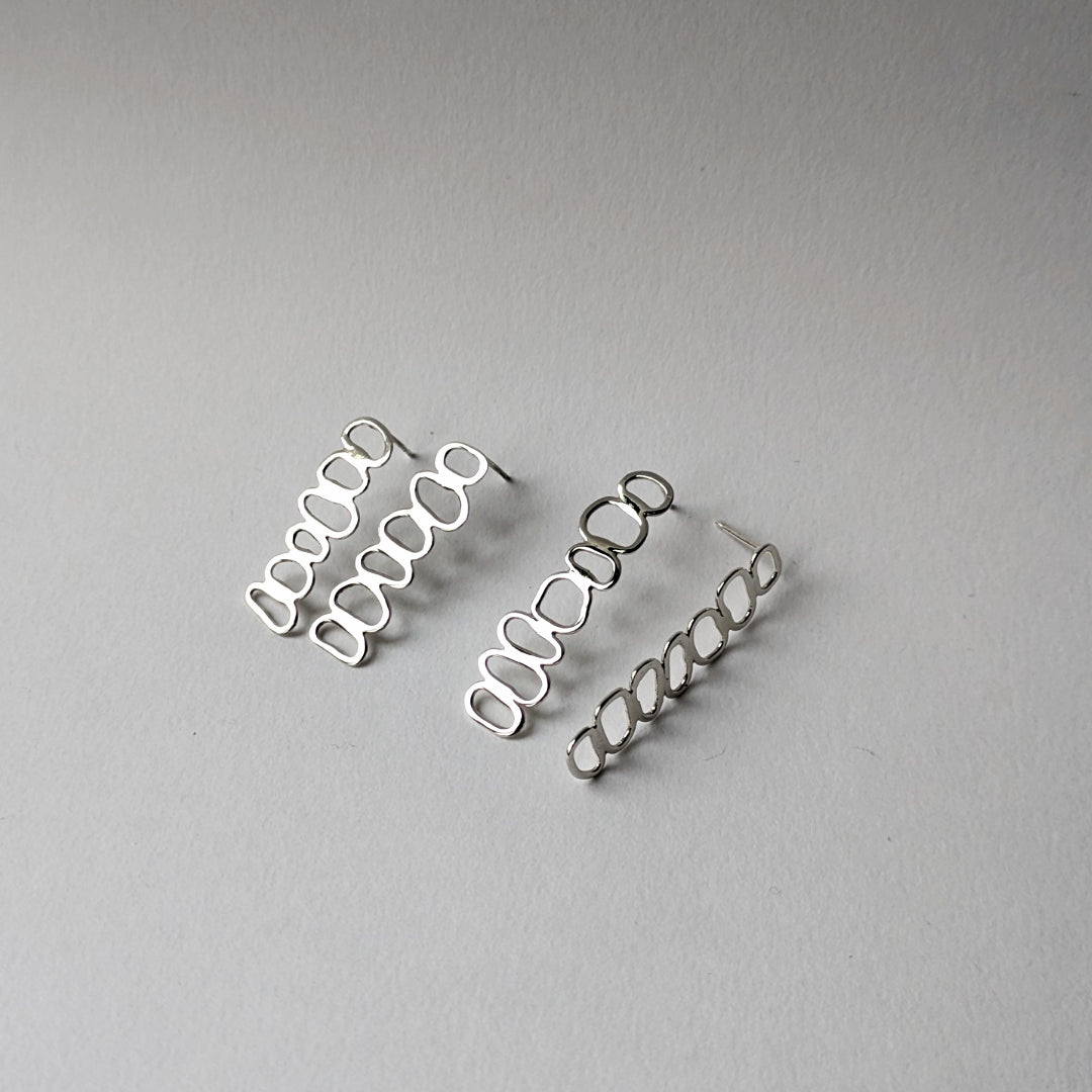 A pair of silver, pebble-shaped, stacked cairn earrings on a grey background