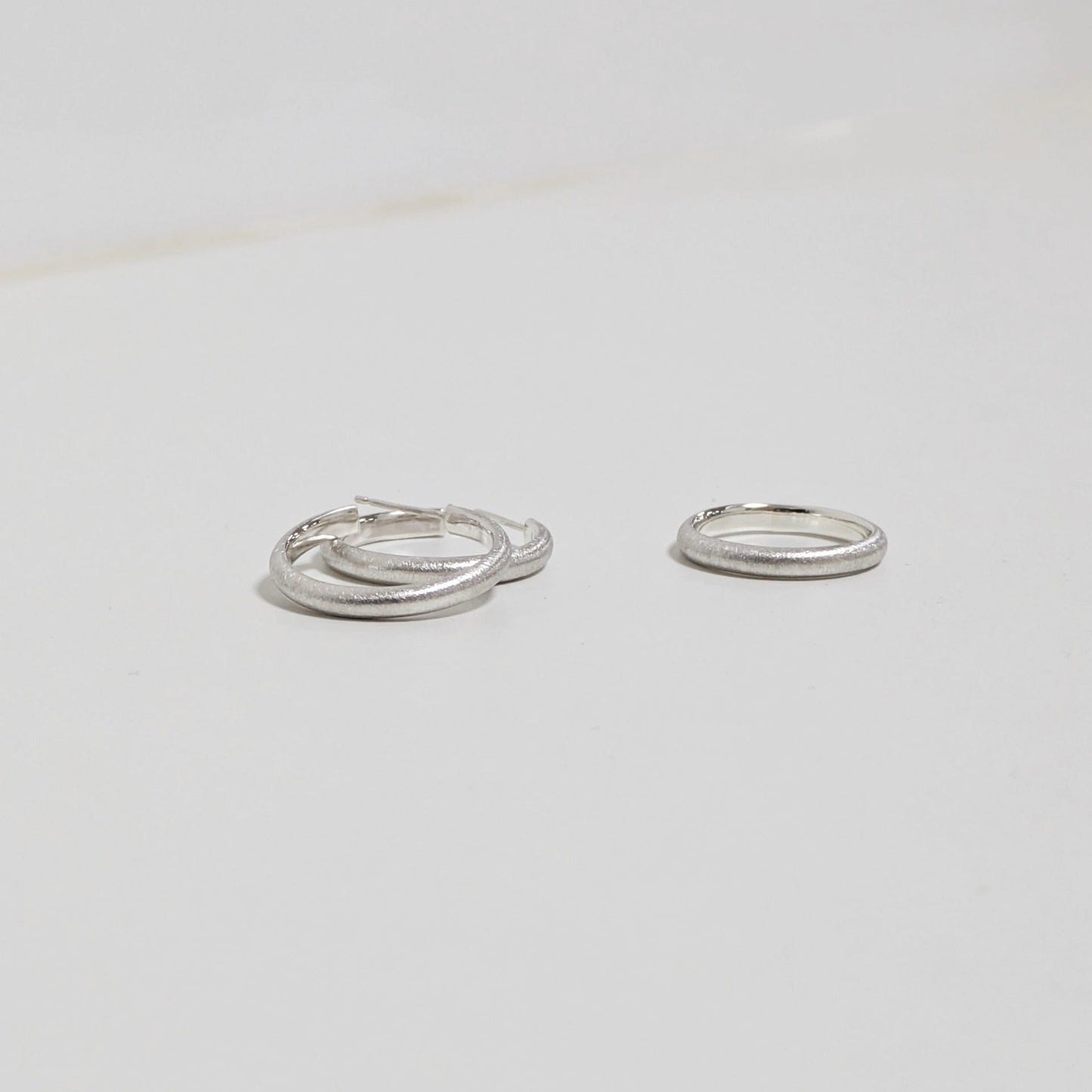 Two satin textured hoops and matching silver ring on white background