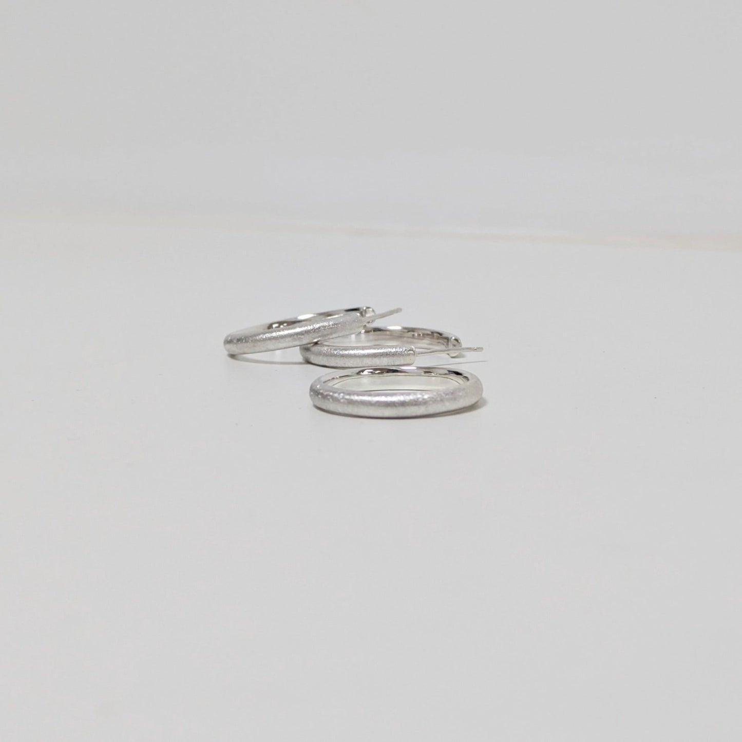 Two satin textured hoops and matching silver ring on white background