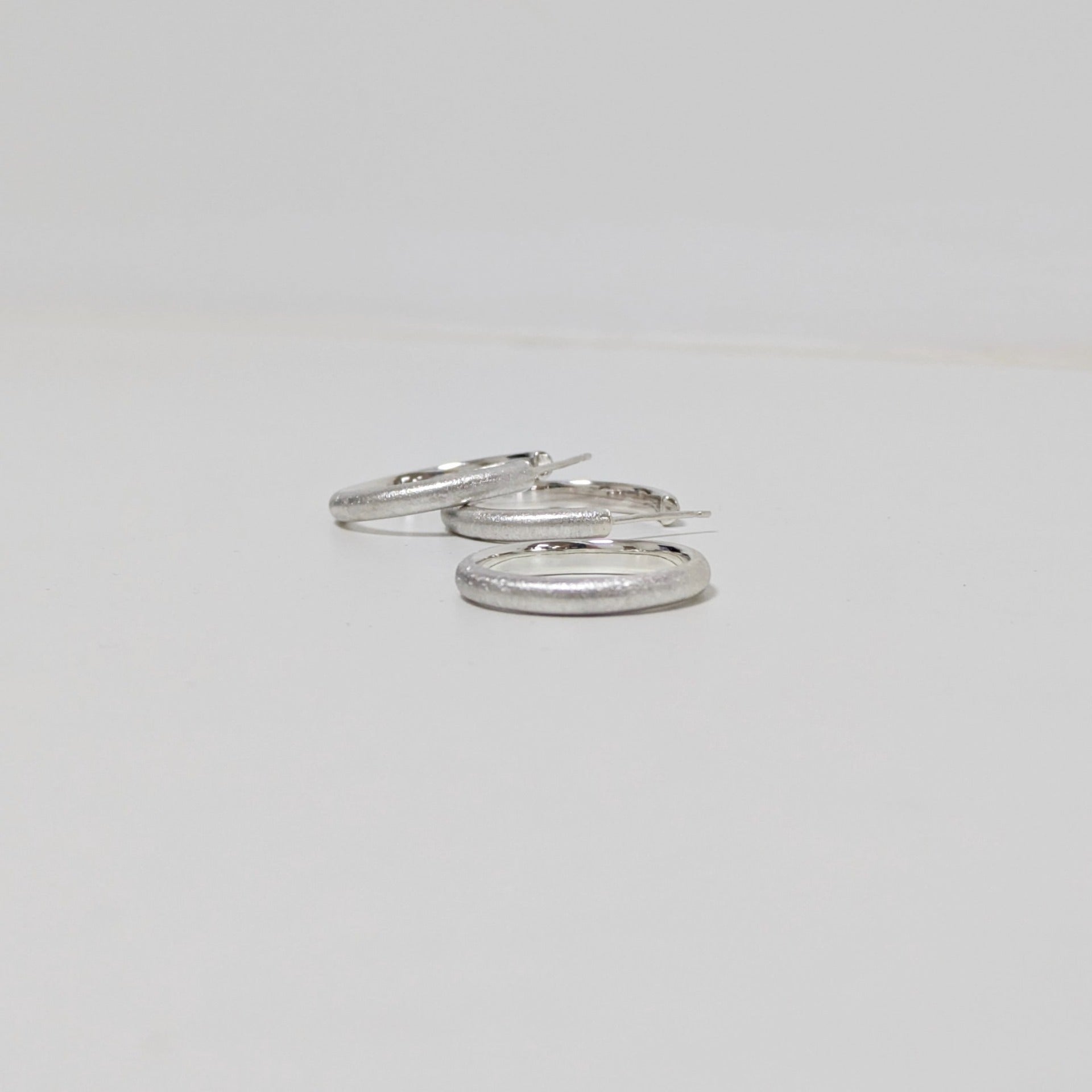 Two satin textured hoops and matching silver ring on white background