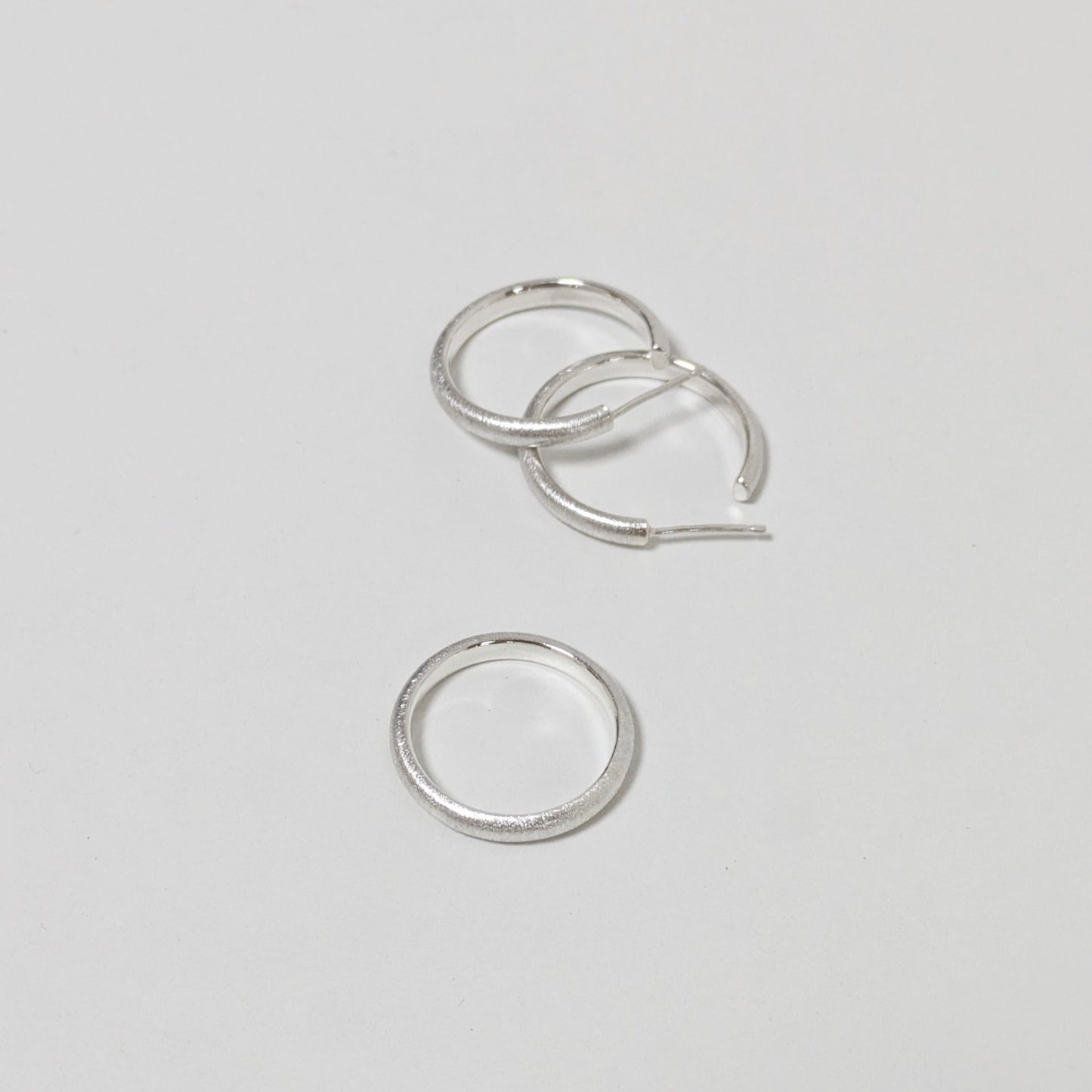 Two satin textured hoops and matching silver ring on white background