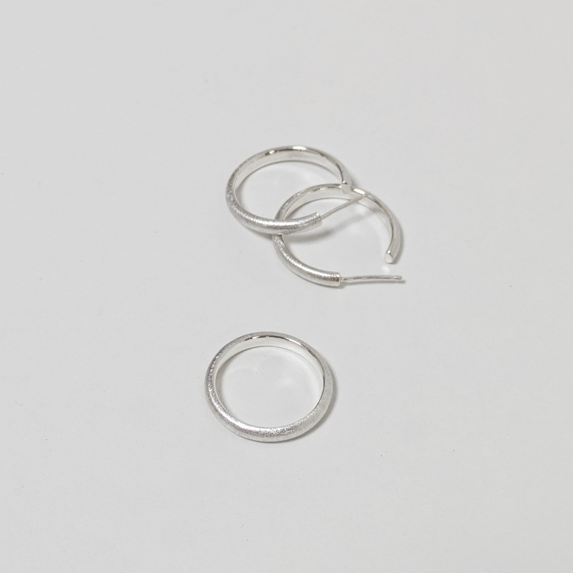 Two satin textured hoops and matching silver ring on white background