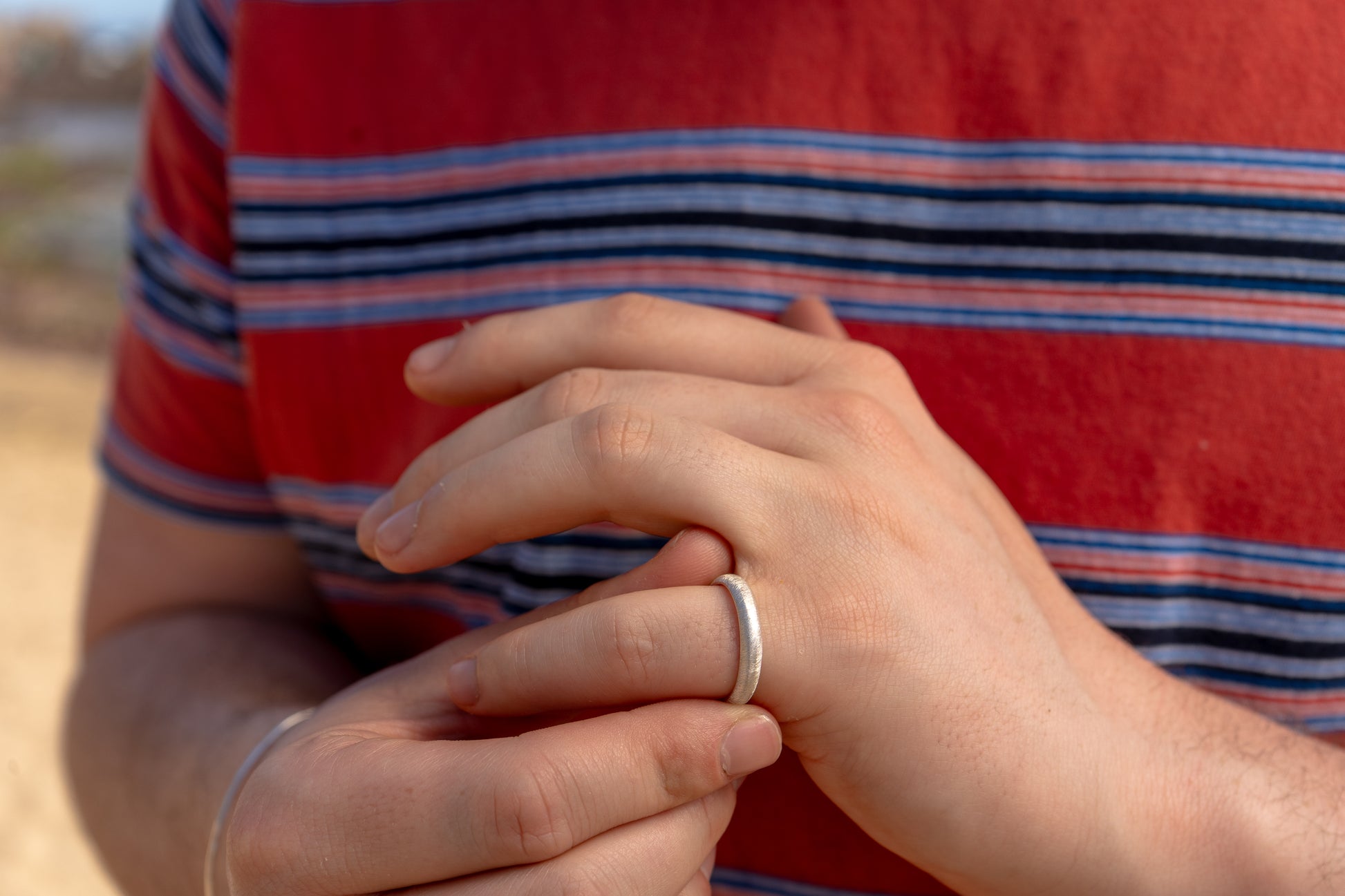 Person wearing a red and blue striped t-shirt with a close-up of hands holding a thin silver textured ring.