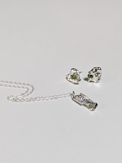 A matching pair of scrap silver earrings and necklace with green sea glass shards embedded, on a light grey background.