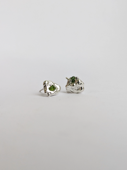 Pair of scrap silver earrings with green sea glass shards embedded, on a light grey background.