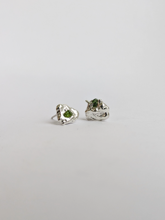 Pair of scrap silver earrings with green sea glass shards embedded, on a light grey background.