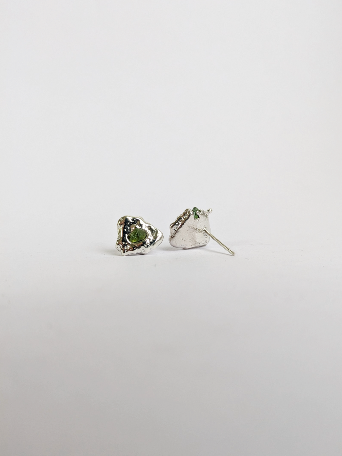 Behind view of a pair of scrap silver earrings with green sea glass shards embedded, on a light grey background.