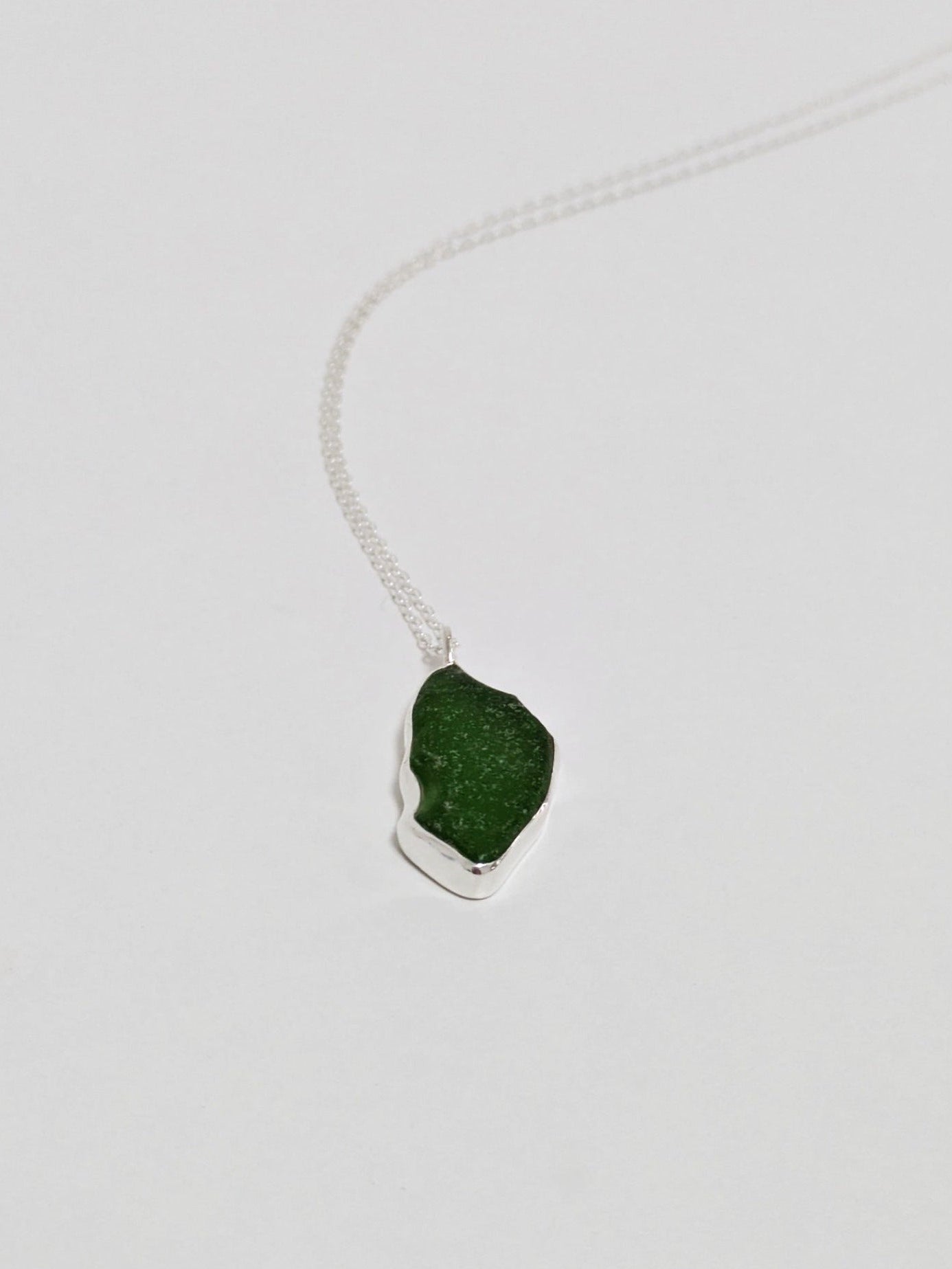 A large green sea glass pendant on a silver chain lies on a white background.