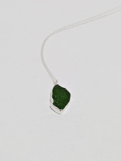 A large green sea glass pendant on a silver chain lies on a white background.