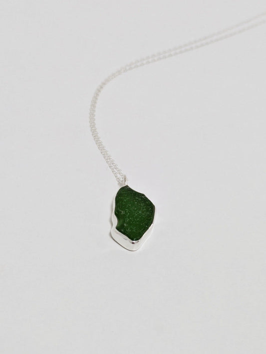 A large green sea glass pendant on a silver chain lies on a white background.