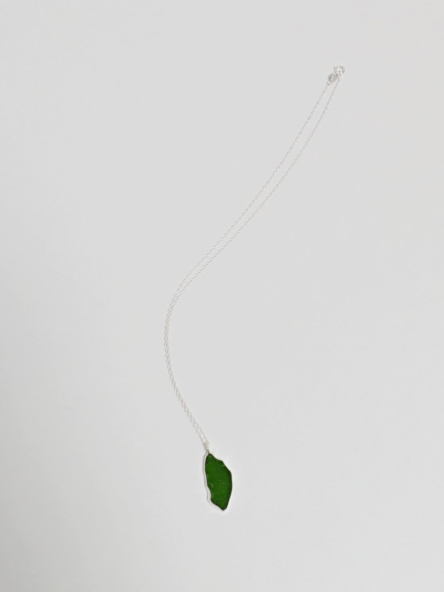 A large green sea glass pendant on a silver chain lies on a white background.