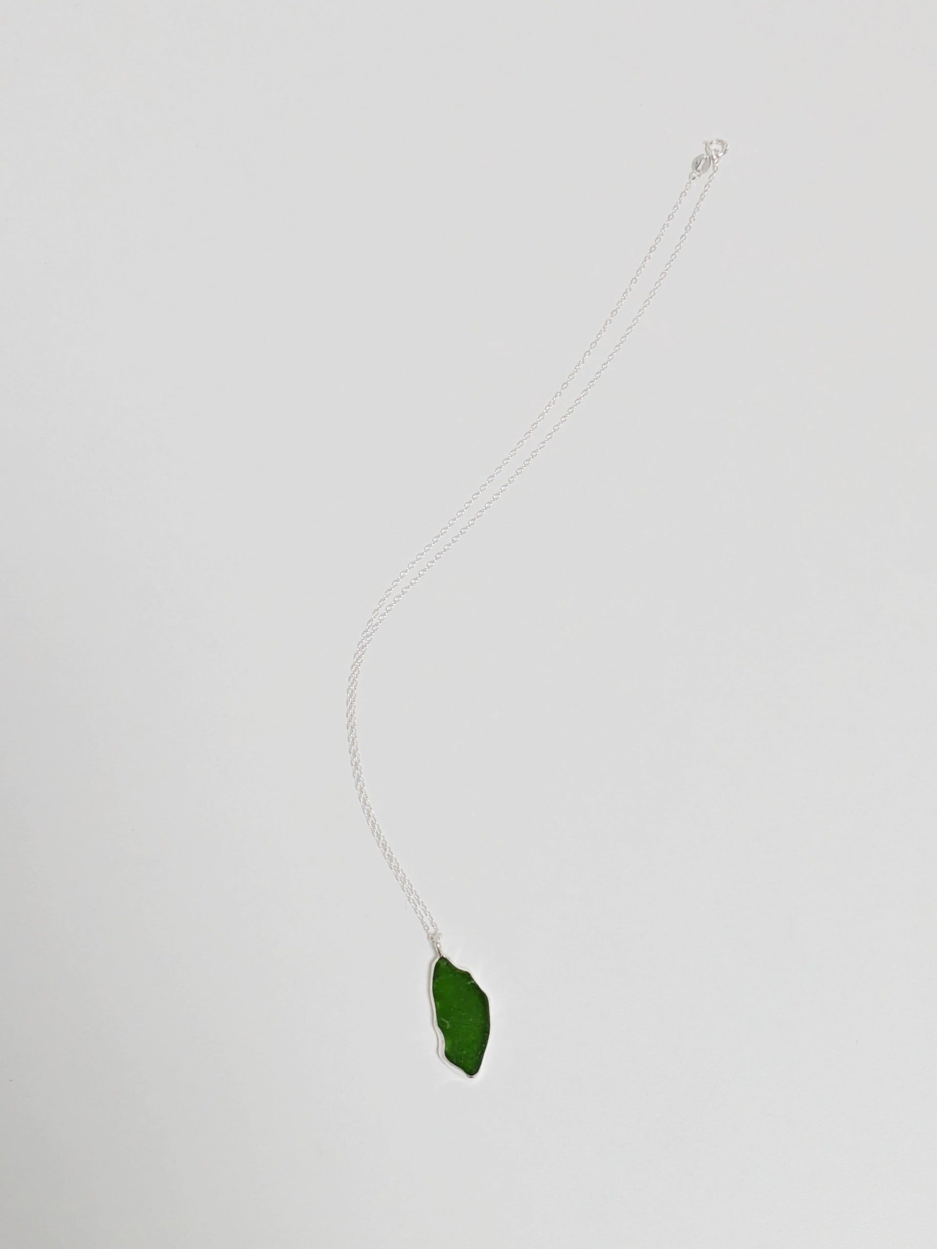 A large green sea glass pendant on a silver chain lies on a white background.