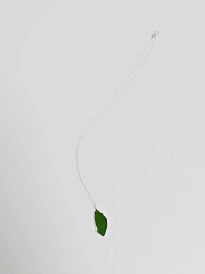 A large green sea glass pendant on a silver chain lies on a white background.