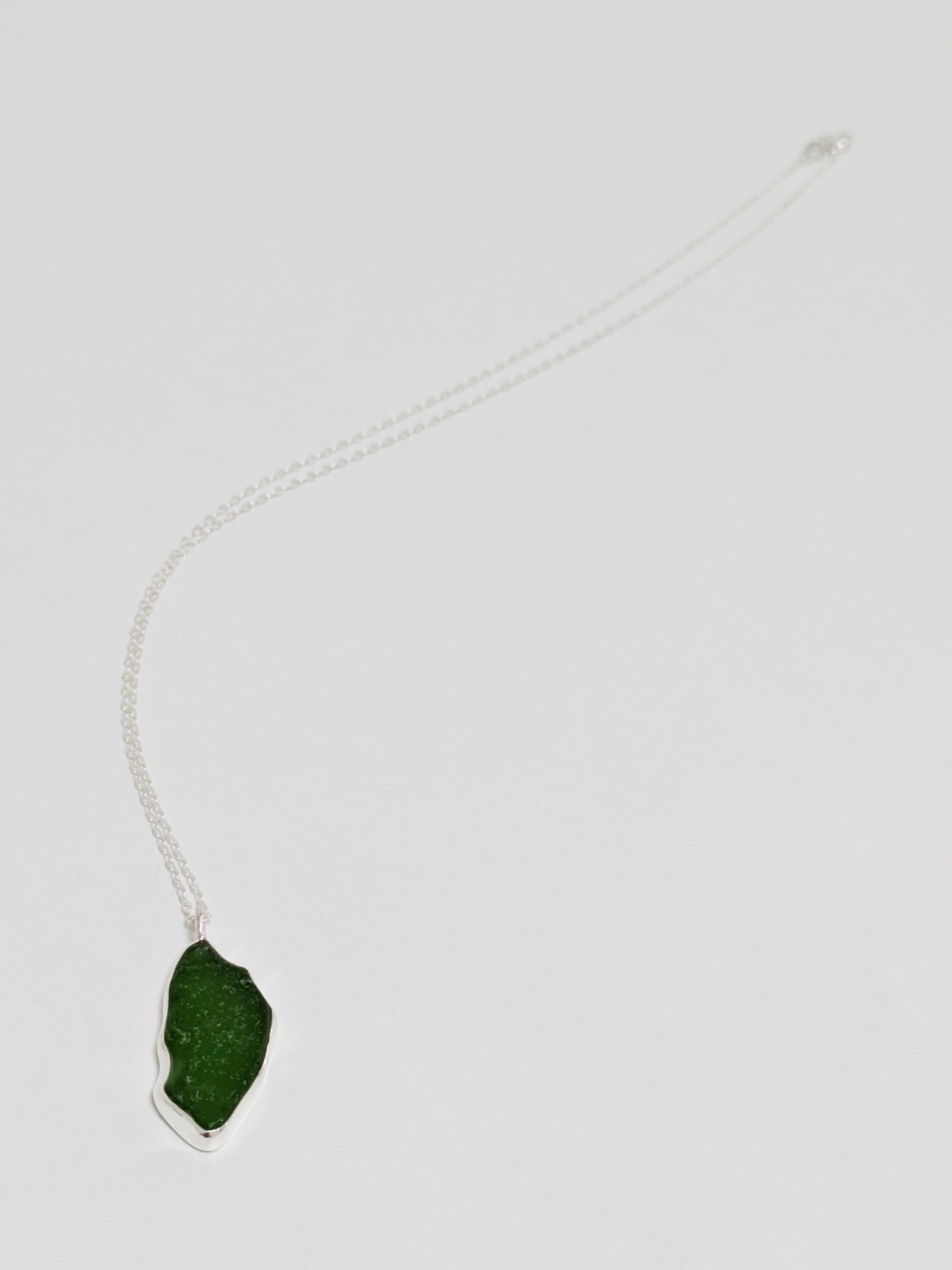 Close up of large green sea glass pendant with a silver chain on a white background.