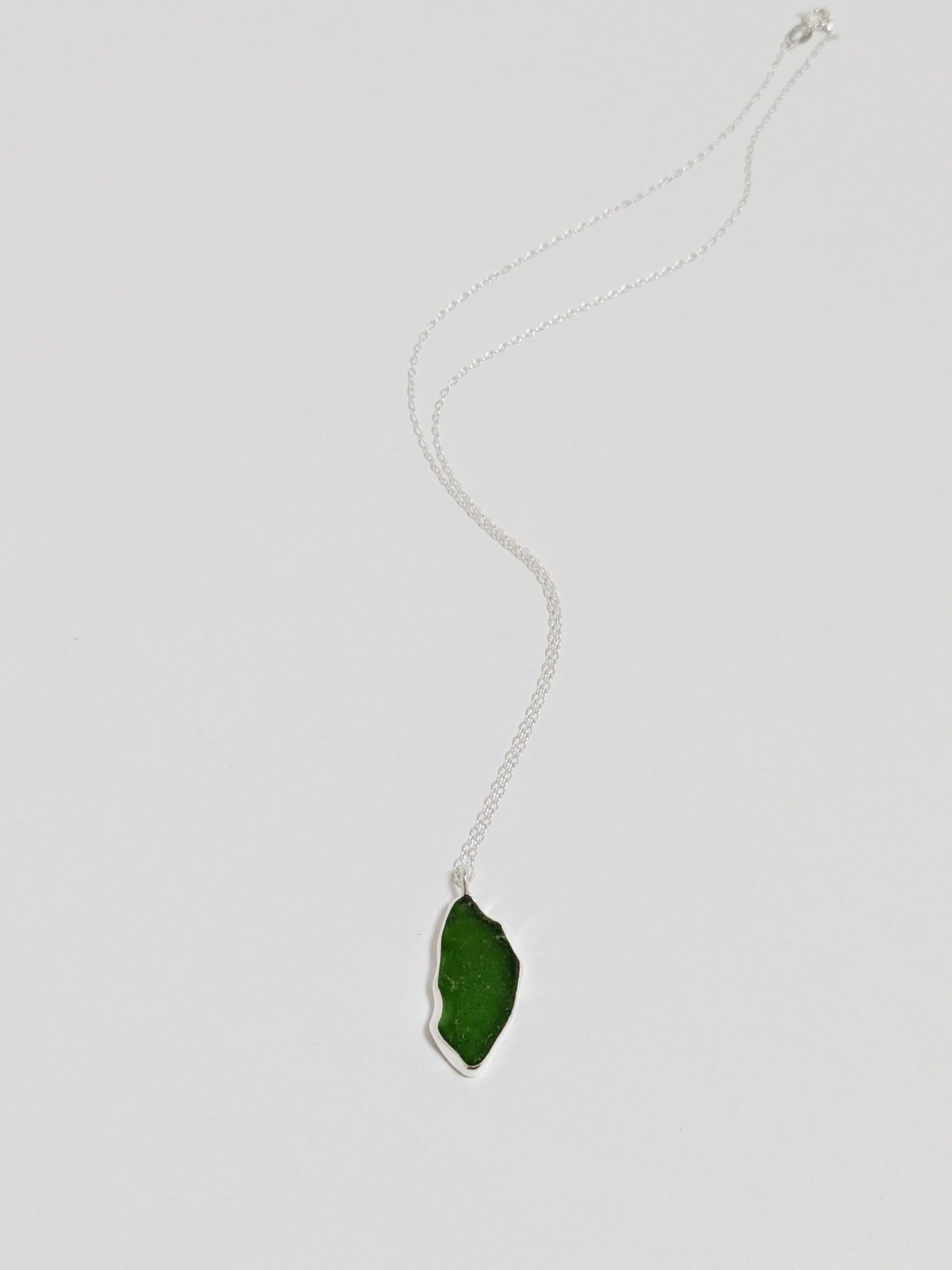 A large green sea glass pendant on a silver chain lies on a white background.