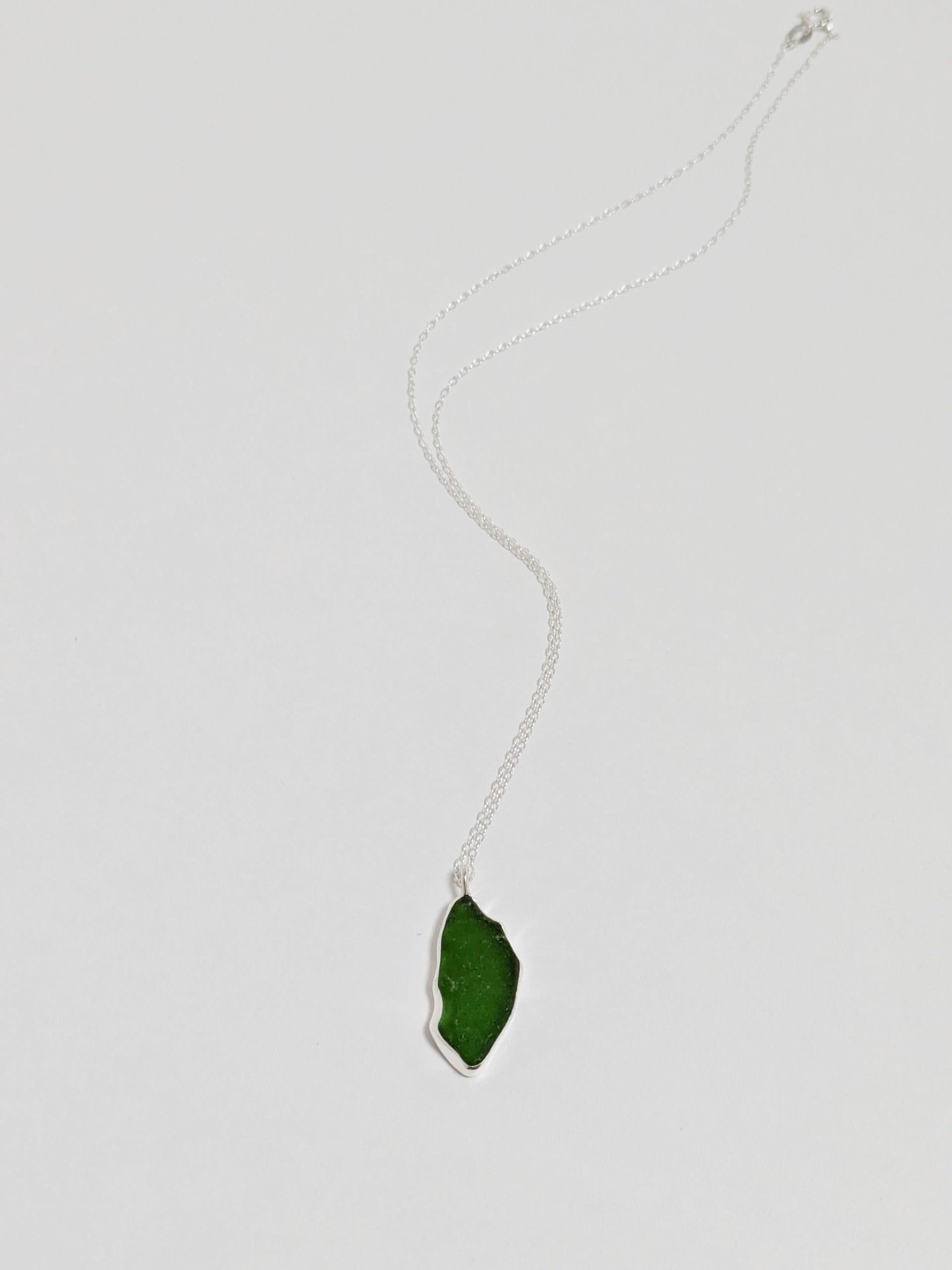 A large green sea glass pendant on a silver chain lies on a white background.