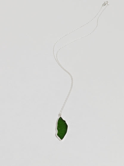 A large green sea glass pendant on a silver chain lies on a white background.