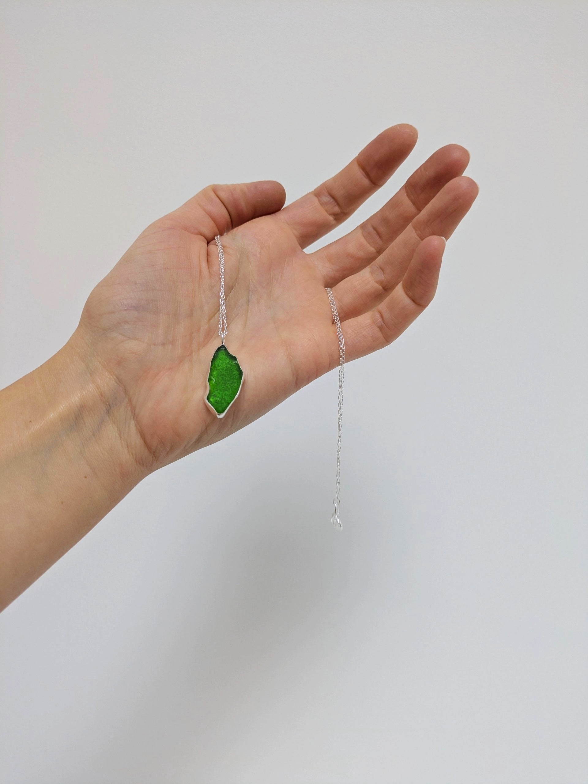 A hand holds a large green sea glass pendant on a silver chain.