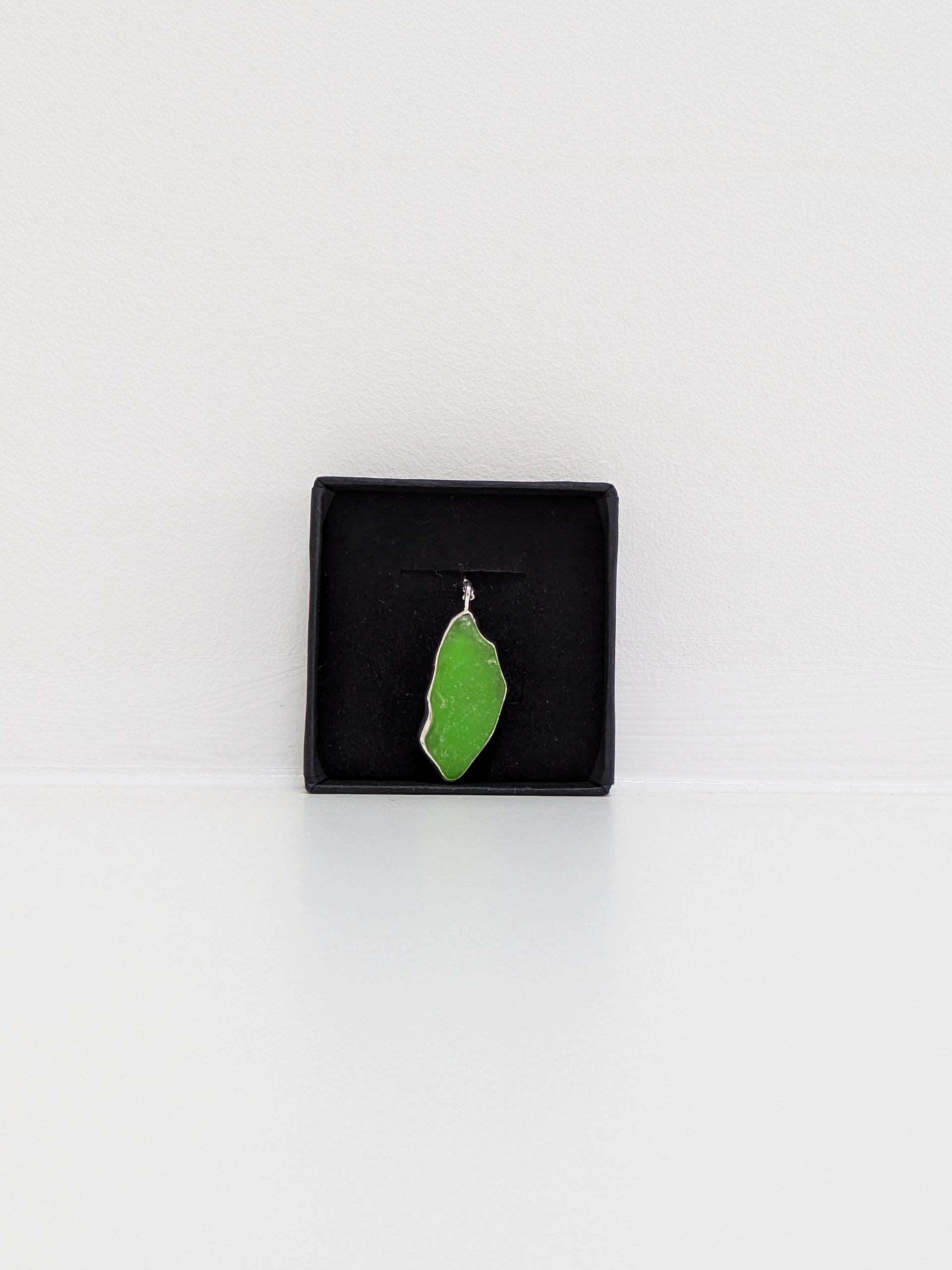 A large green sea glass pendant is in a black display box with a white background.
