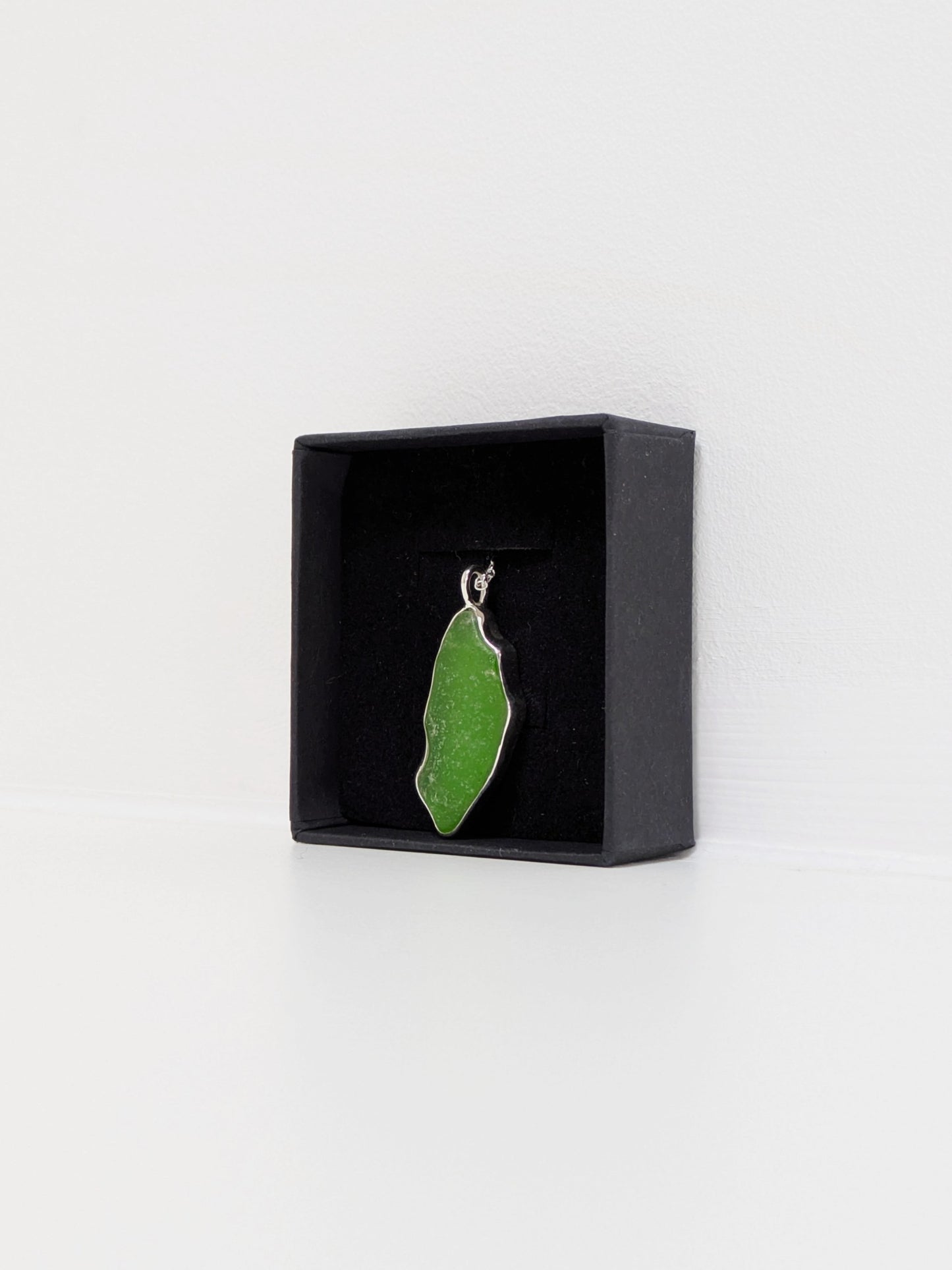 Side view of a large green sea glass pendant in a black display box with a white background.