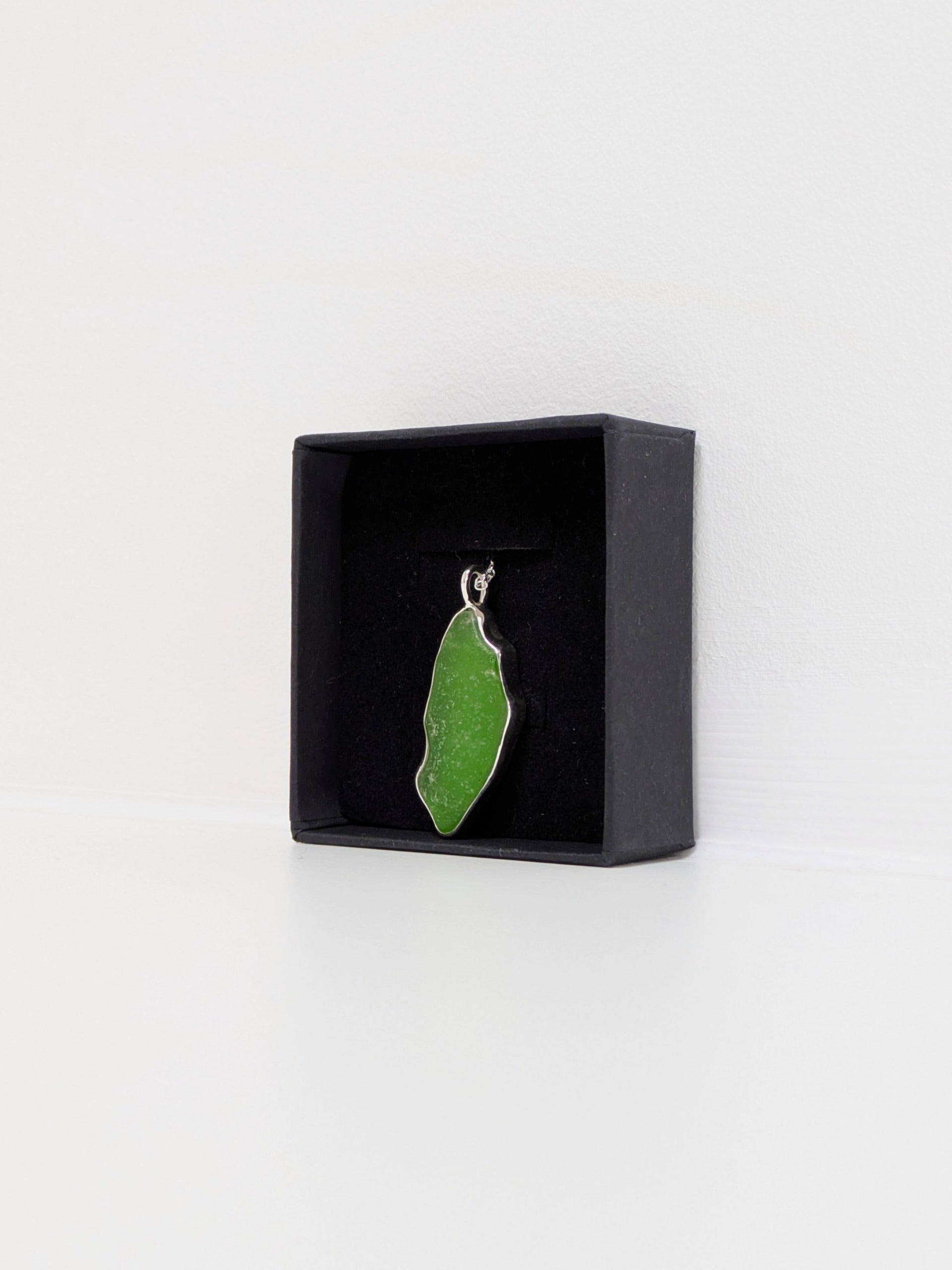 Side view of a large green sea glass pendant in a black display box with a white background.