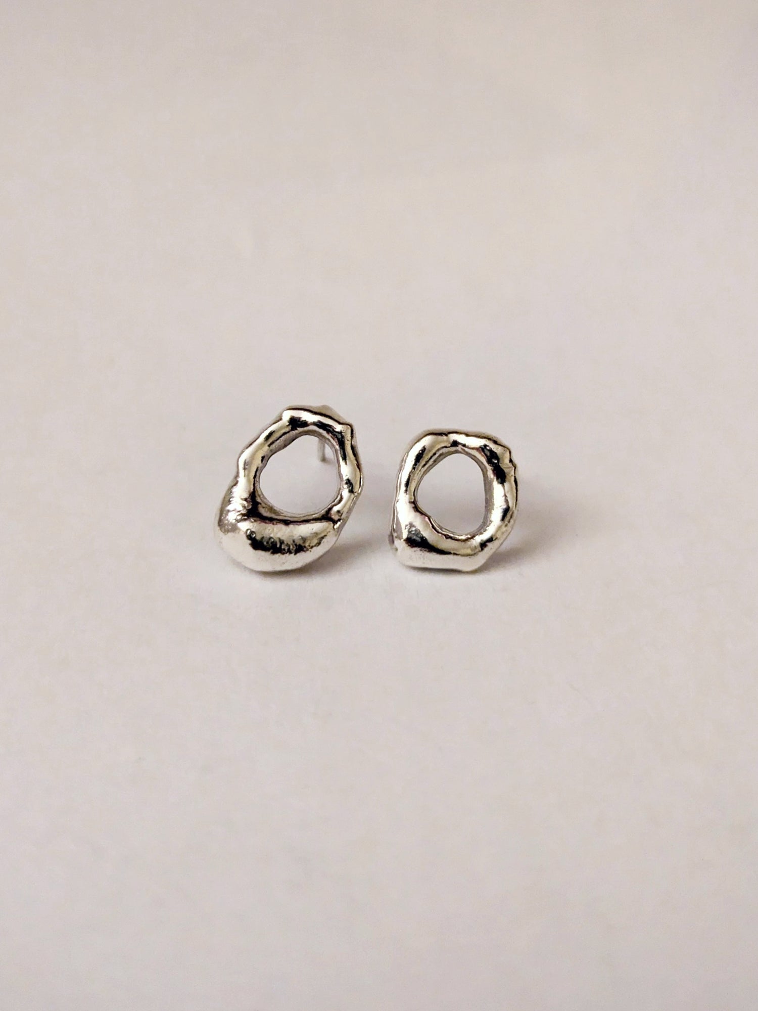 Pair of silver mini molten earrings on a light beige background