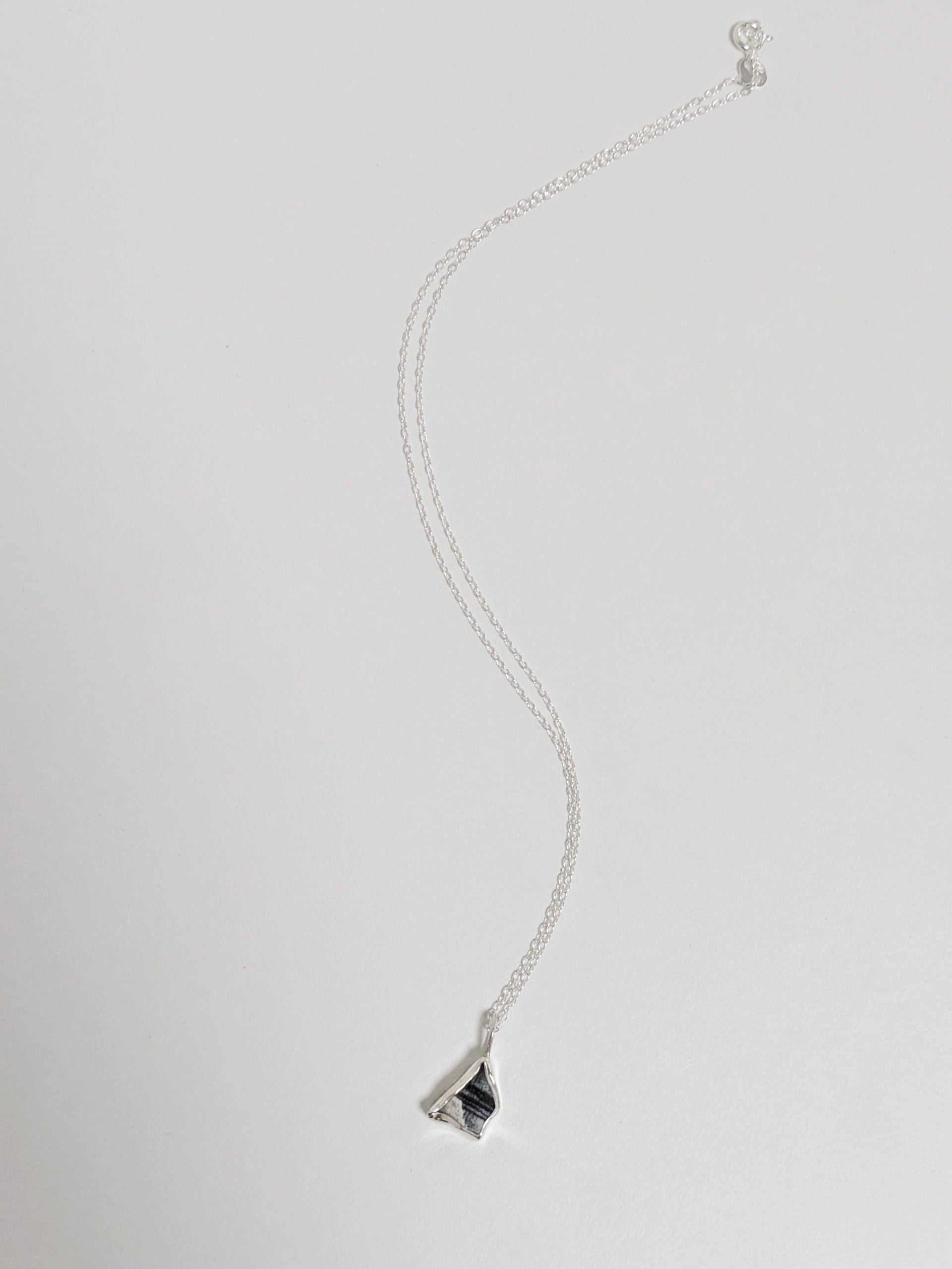 Mini black and white sea pottery pendant with a thin silver chain lying on a white background.