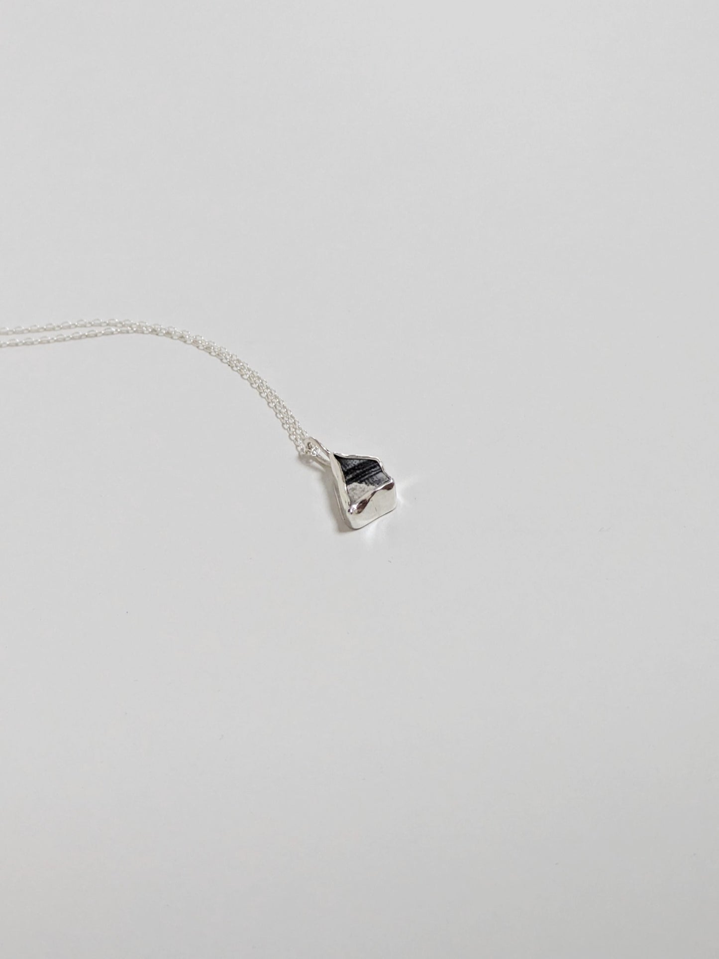 Mini black and white sea pottery pendant with a thin silver chain at an angle on a white background.