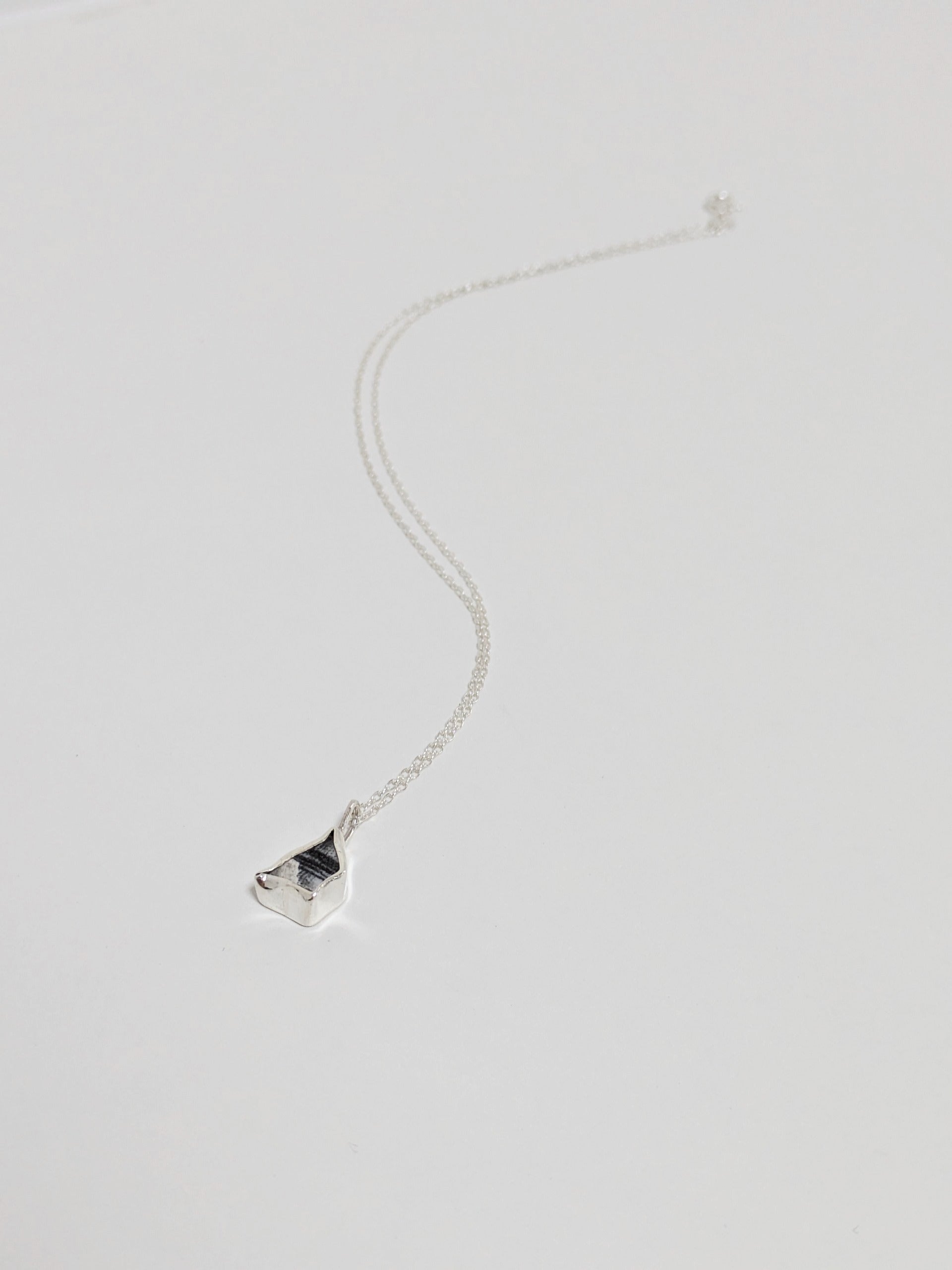 Mini black and white sea pottery pendant with a thin silver chain on a white background.