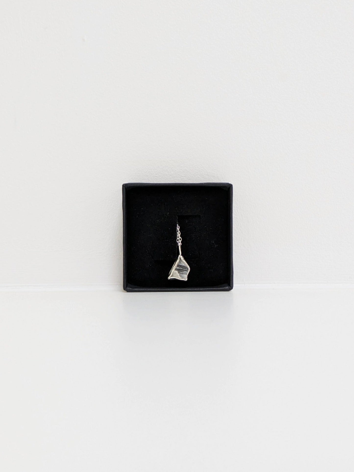 Mini black and white sea pottery pendant with a thin silver chain in a black display box on a white background.