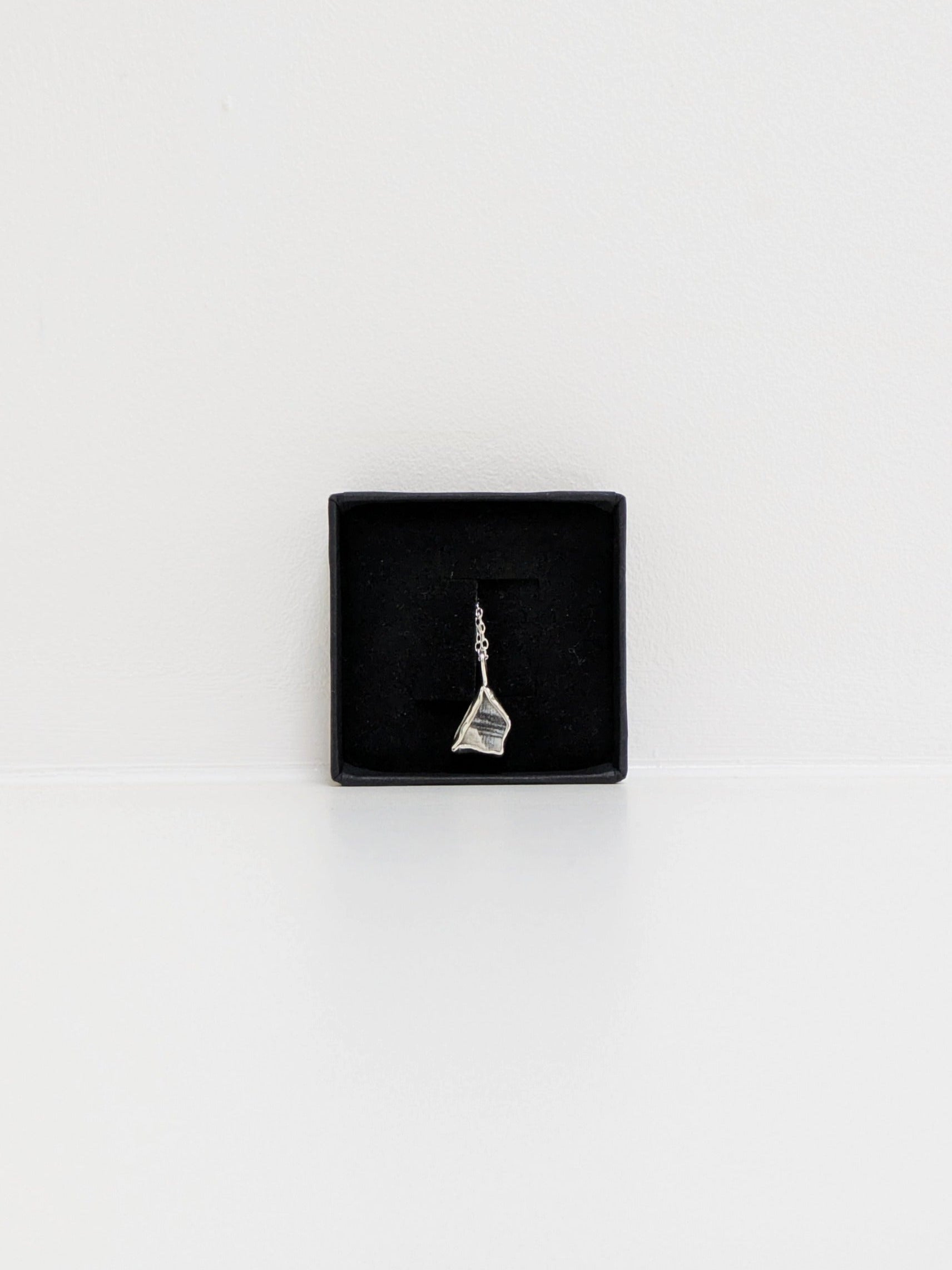 Mini black and white sea pottery pendant with a thin silver chain in a black display box on a white background.