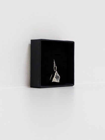 Side view of a mini black and white sea pottery pendant with a thin silver chain in a black display box on a white background.