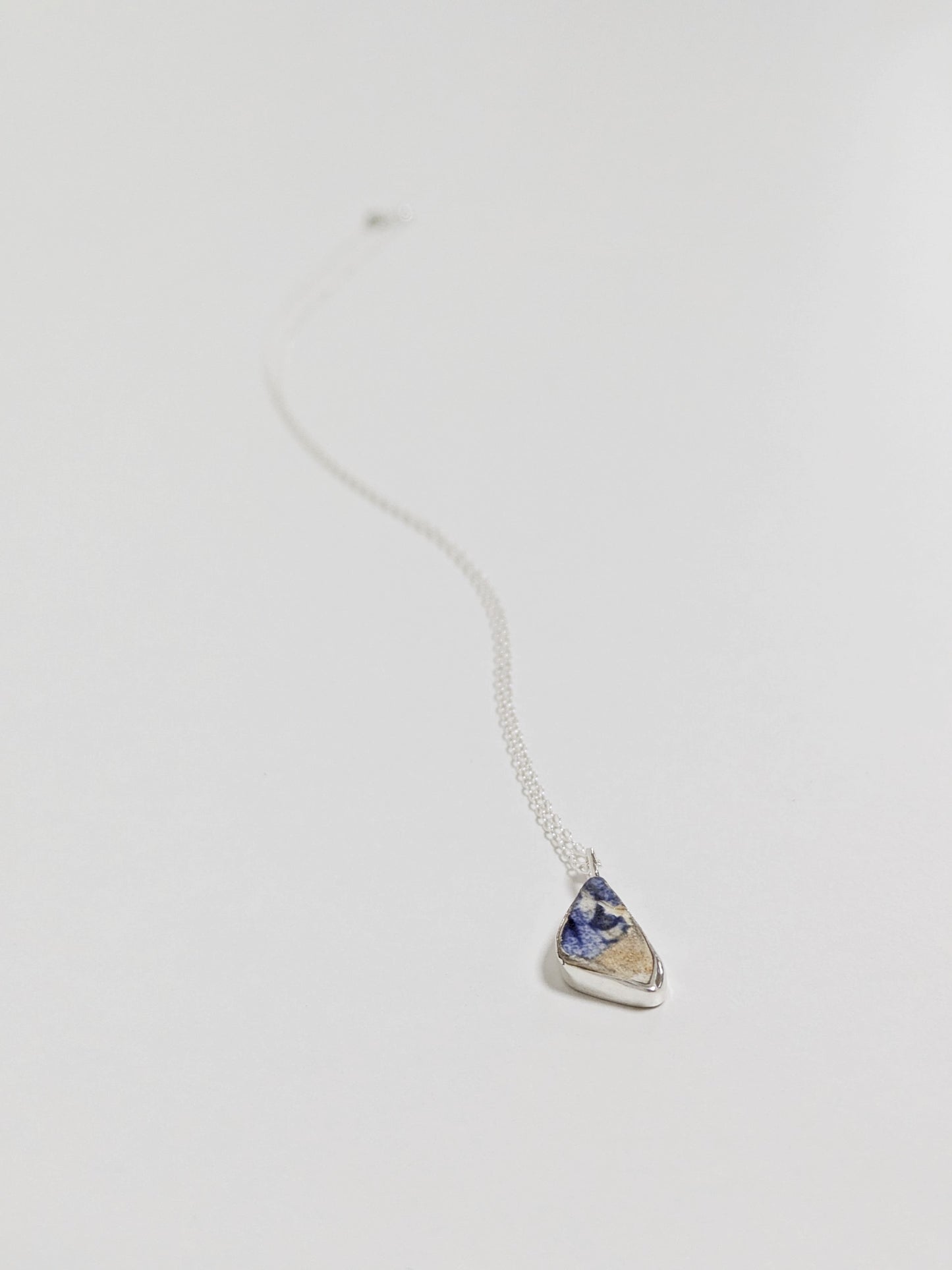 Close up of mini blue and white sea pottery necklace on white background.