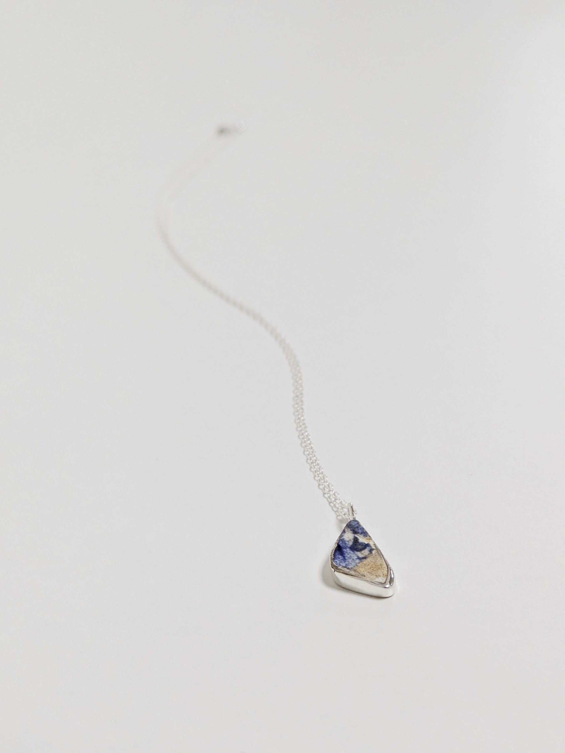 Close up of mini blue and white sea pottery necklace on white background.