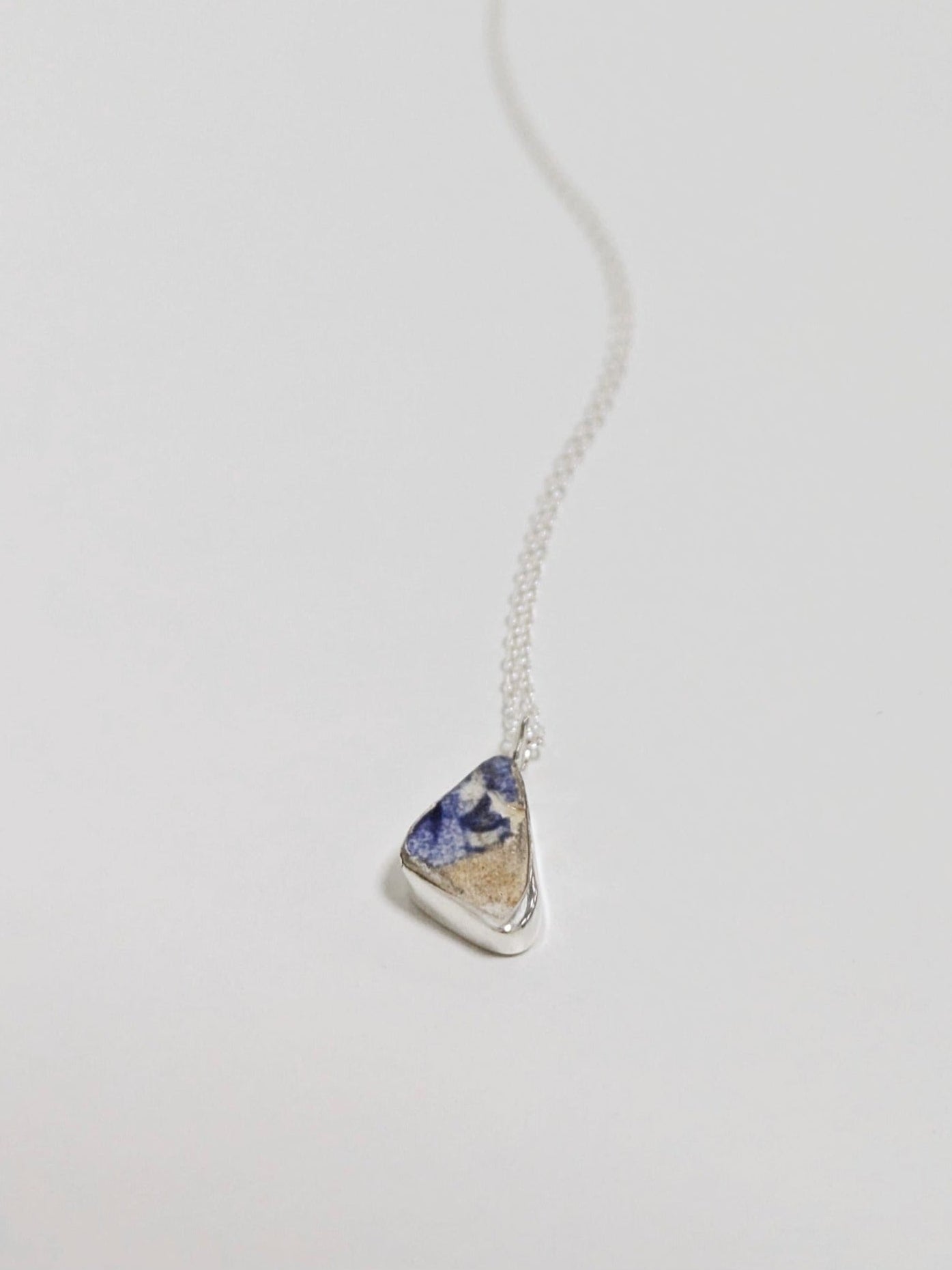 Close up of mini blue and white sea pottery necklace on white background.